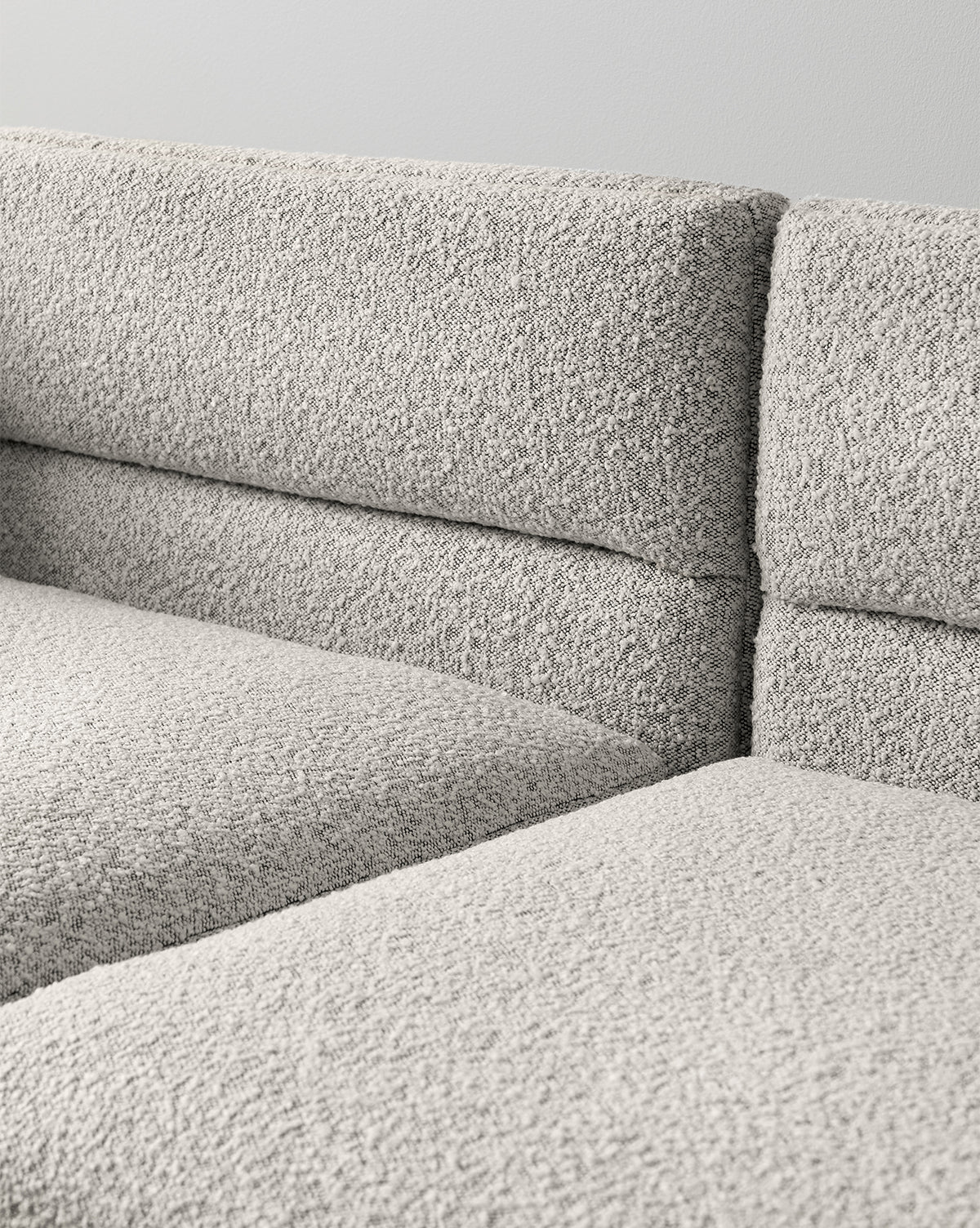 Close-up view of the Makerspalm Claremont Modular Sofa 99 in textured light gray fabric, featuring clean lines and a minimalist design against a plain light-colored wall. McGee & Co.