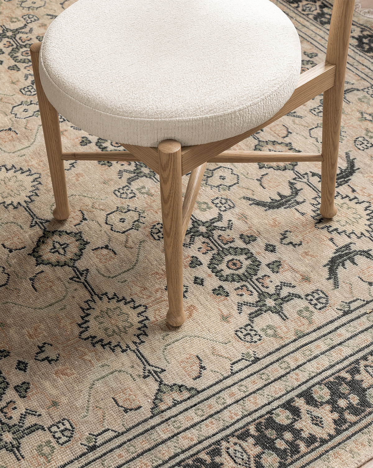 The Garance Dining Chair, featuring white oak and a round white cushioned seat, is placed on a beige and black rug with floral and geometric patterns, by McGee & Co.