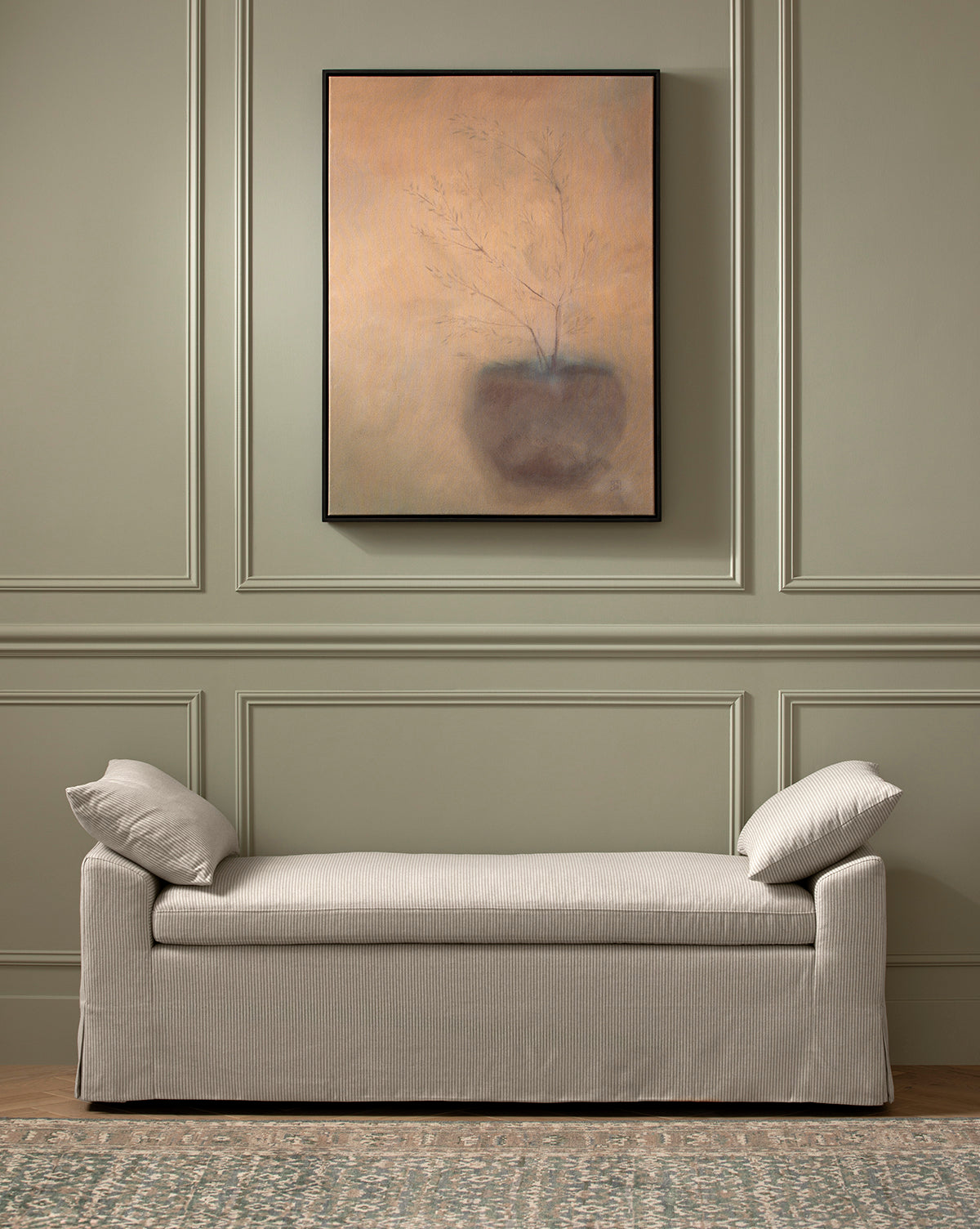 A minimalist room with green paneled walls, a soft beige bench with cushions, and Olive by Jess Engle—a framed botanical artwork—hanging above.