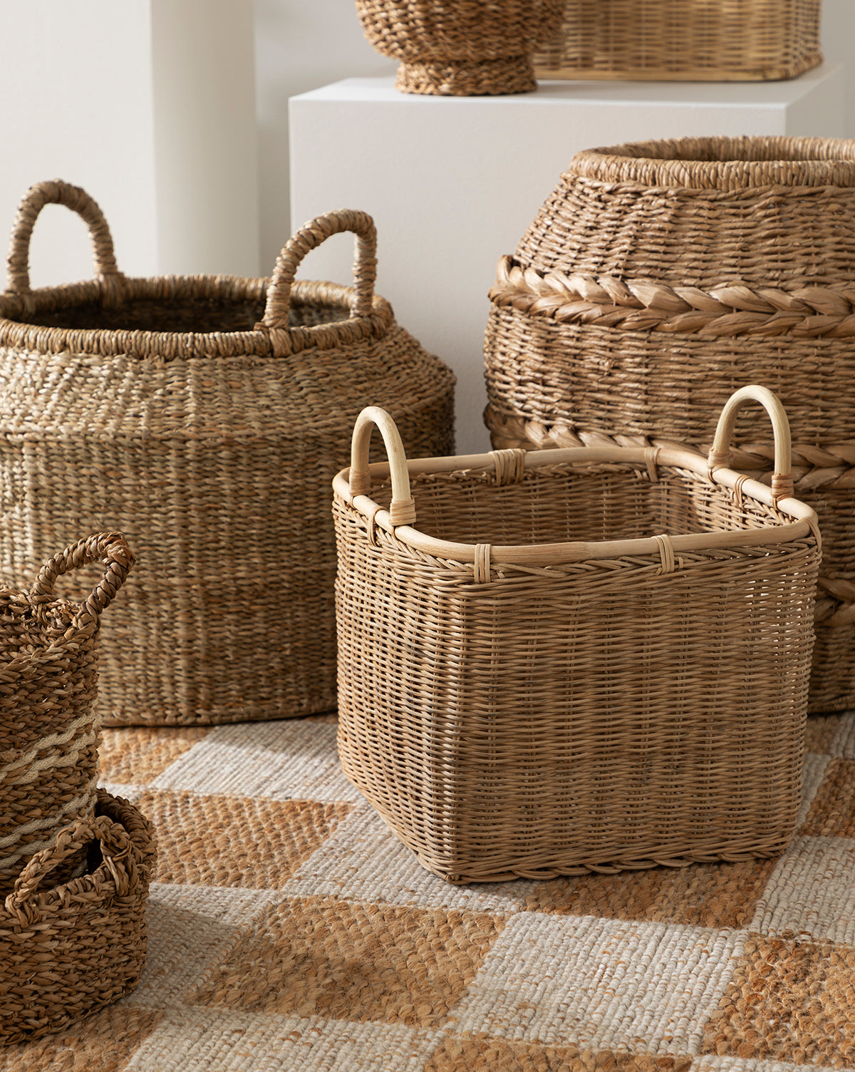 The Liesl Basket, made from natural mendong grass, is arranged on a patterned rug. Its handles and organic hues create a cozy, rustic feel in the space, by McGee & Co.
