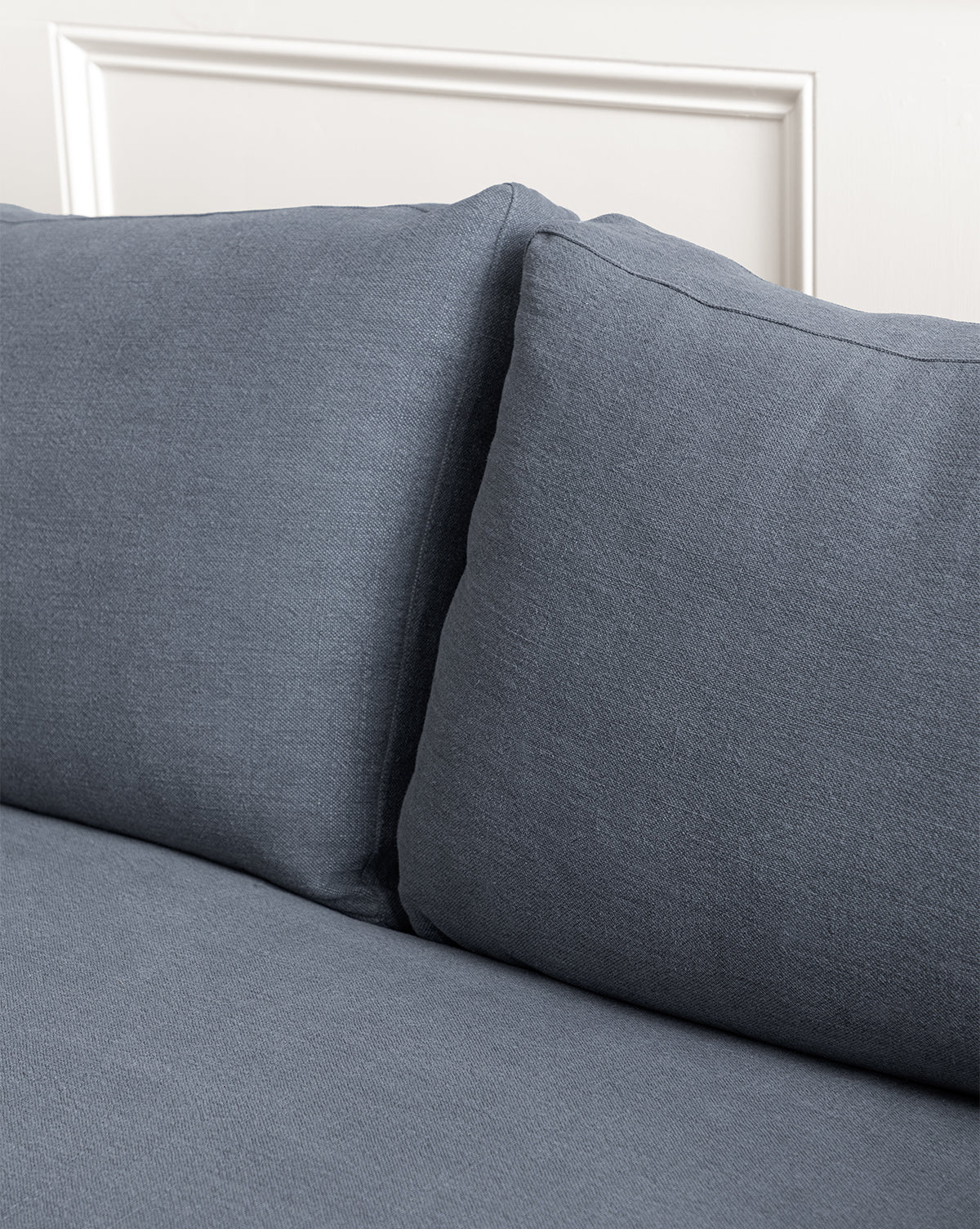 Close-up of the Peterson Classic Upholstered Sofa (75 - 100) featuring two large, plush blue-gray back cushions and a matching seat cushion, set against a white paneled wall, by McGee & Co.