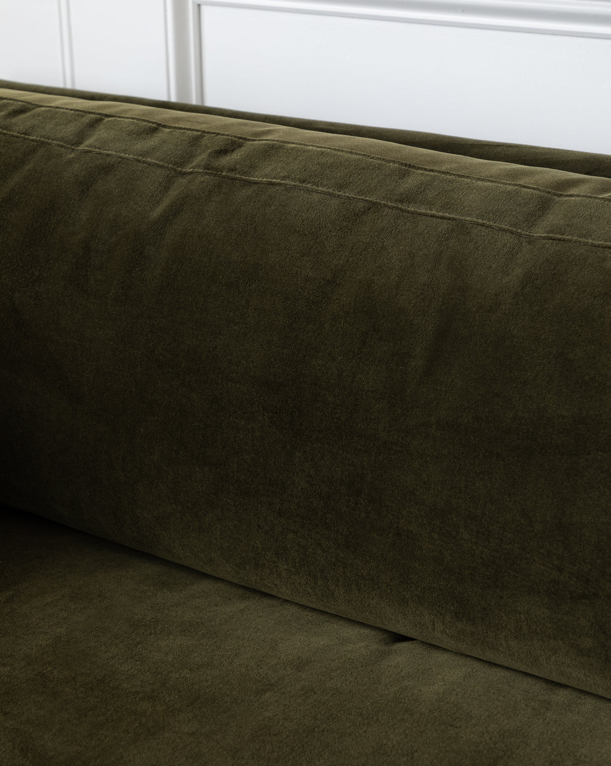 Close-up of the deep green Haverford Upholstered Sofa 90 backrest and seat, featuring subtle stitching details, set against a white paneled wall, by McGee & Co.