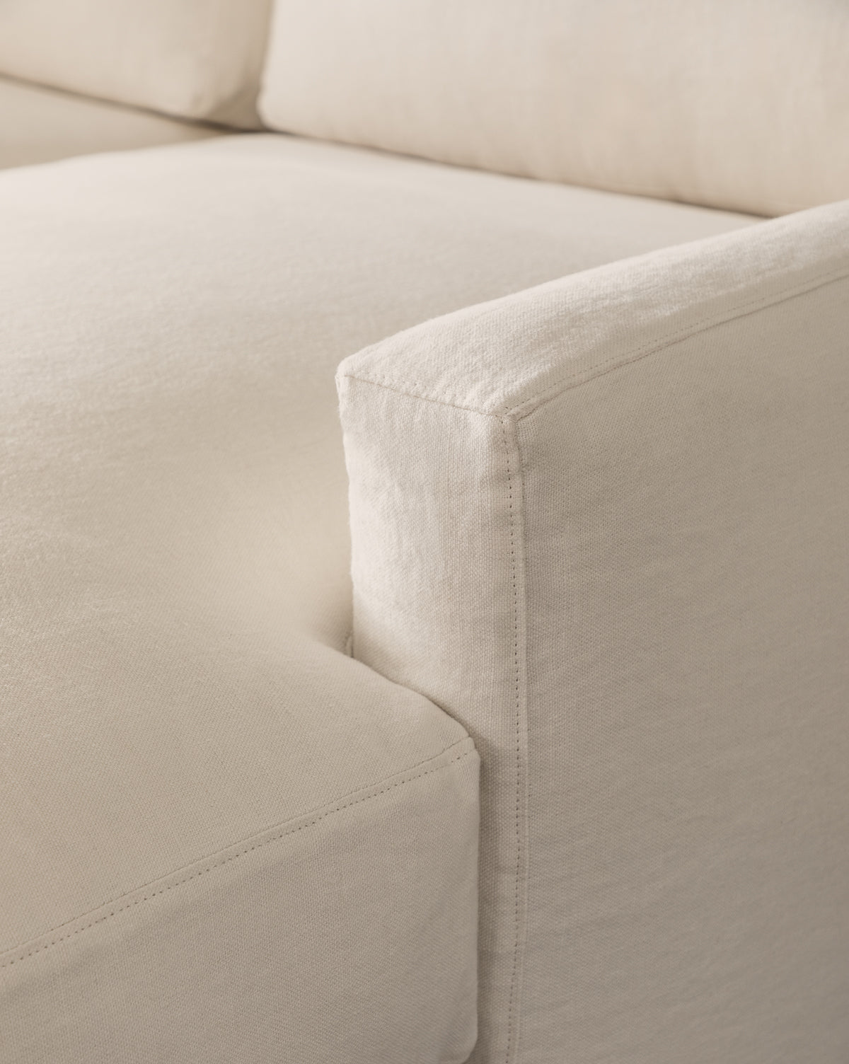 Close-up view of the Community Macy Slipcover Chaise Sectional 101 in beige, highlighting the seat cushion, armrest, and backrest with visible stitching and a soft, textured surface—McGee & Co.