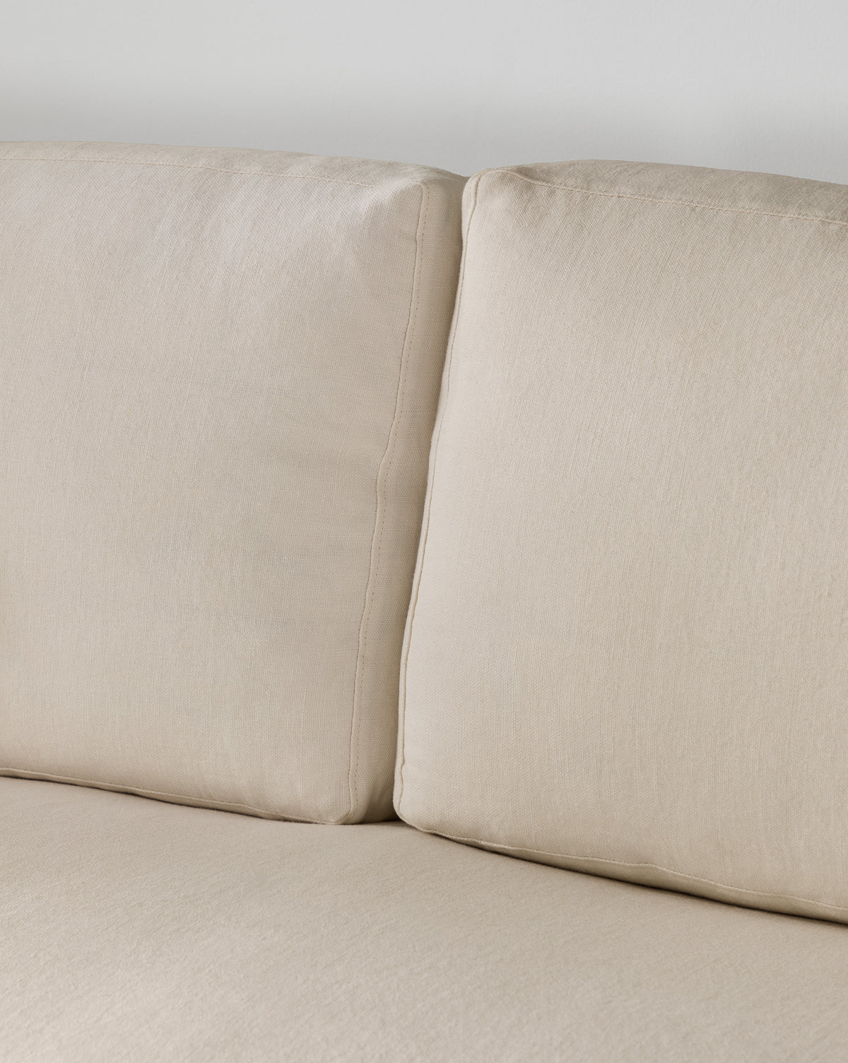 Close-up of two beige sofa cushions with a visible seam, set against a light wall. These soft, textured cushions are part of the Community Macy Slipcover Chaise Sectional 101 by McGee & Co.