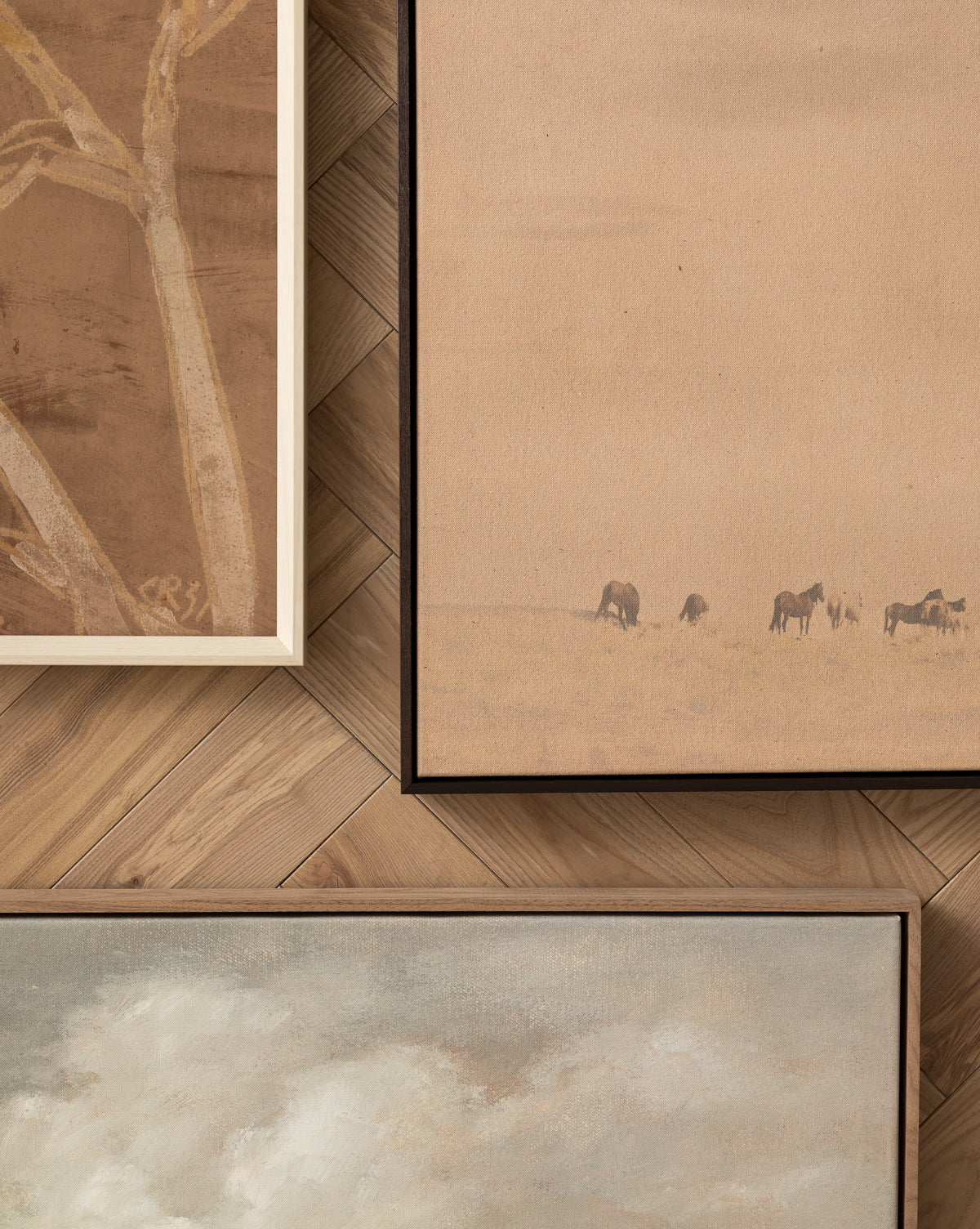 The Smokey Pasture giclee print features three framed wall art pieces with earth tones: abstract tree branches, grazing horses in a rural scene, and a cloudy sky, all displayed on a herringbone wood wall by McGee & Co.