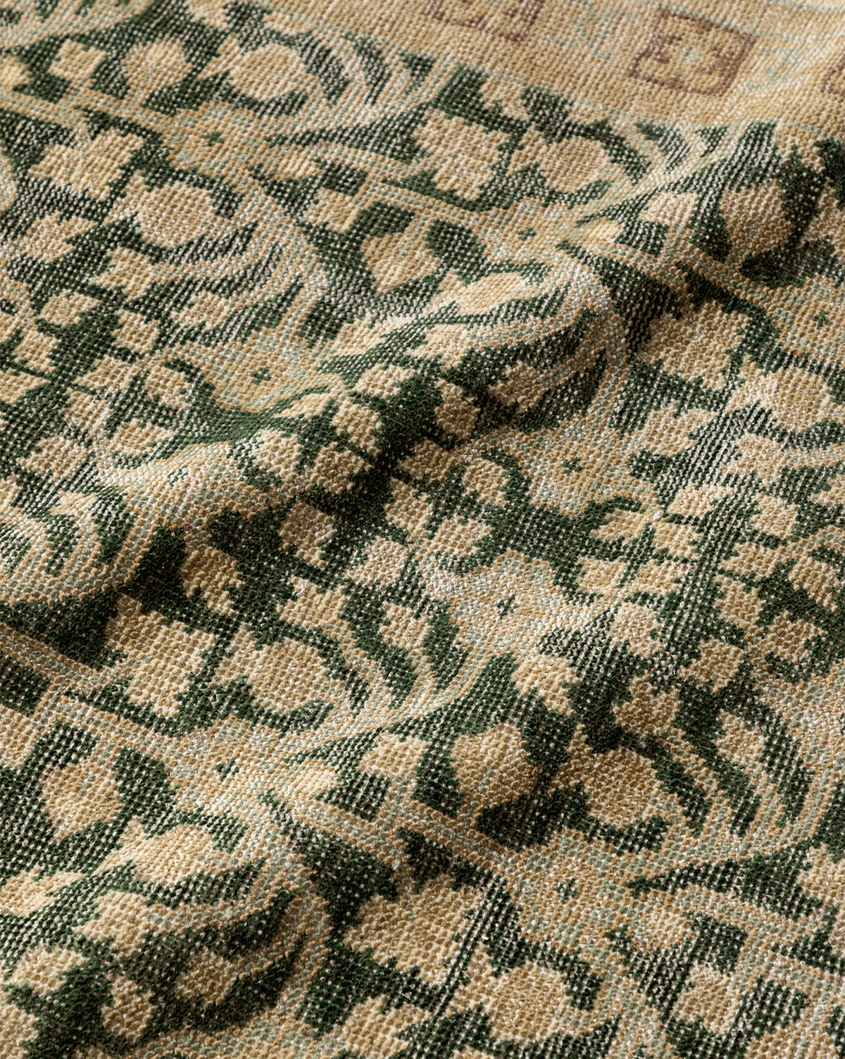 Close-up of the Evangeline Hand-Knotted Wool Rug, showcasing its intricate green and beige floral pattern, visible texture, and gentle folds that highlight the timeless charm of this vintage-inspired piece, by McGee & Co.