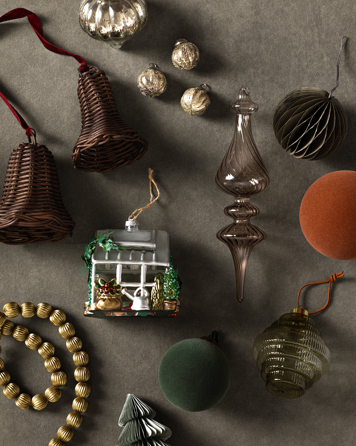 Flocked Baubles (Set of 8) are arranged on a gray surface with wicker bells, gold baubles, a glass house, textured and smooth ornaments, velvet balls, a paper tree, and a gold bead garland for festive holiday decor, by McGee & Co.