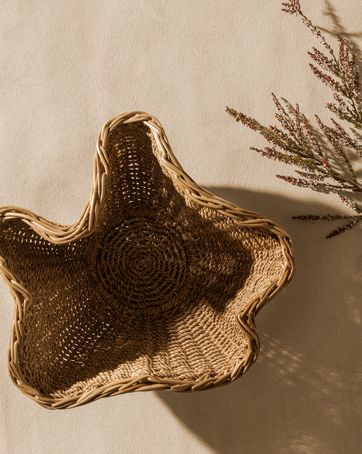 The Goulding Woven Bowl, shaped like a star, rests on a beige surface beside delicate flowers casting soft shadows—ideal as charming entryway decor, by McGee & Co.