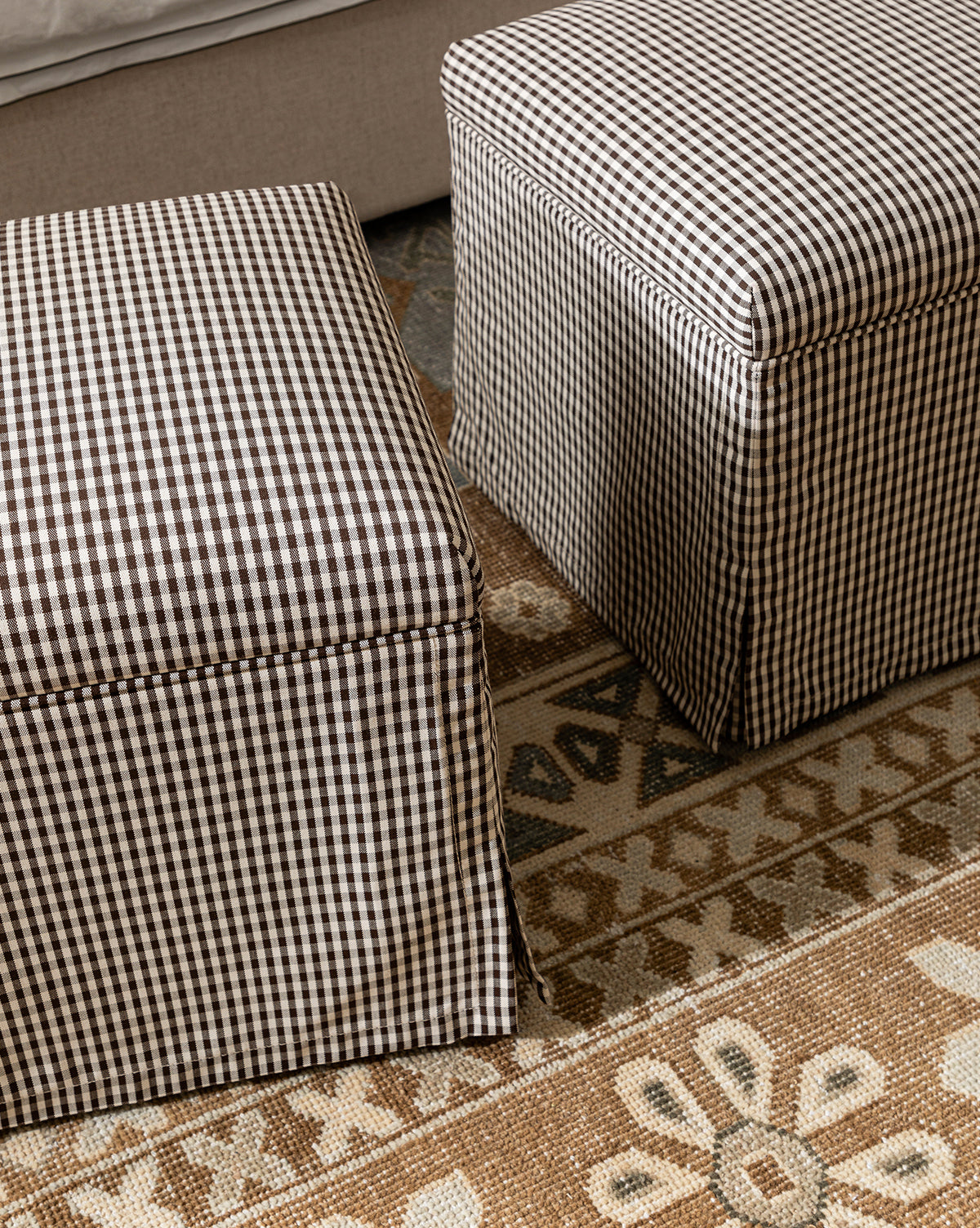 Two Makerspalm Latimer Ottomans (Ready to Ship) with black and white gingham fabric rest on a patterned beige and brown rug next to a light sofa, offering stylish, functional accent seating by McGee & Co.