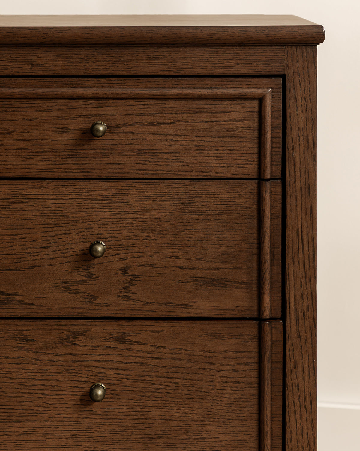 Close-up of the upper half of the Yorkshire Dresser with three drawers, featuring an English oak finish and round metal knobs, by McGee & Co. Visible wood grain enhances its elegant storage design against a light-colored wall.