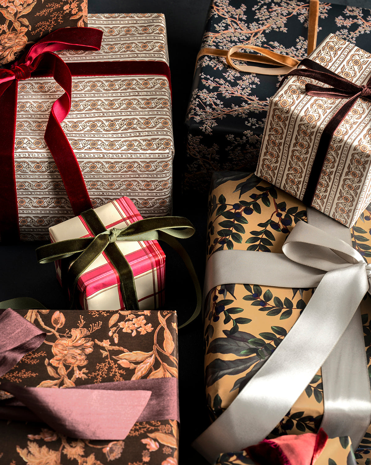 A set of Foragers Gift Wrap presents, beautifully wrapped in floral, striped, and leafy designs with colorful ribbons, arranged closely together against a dark background, by McGee & Co.