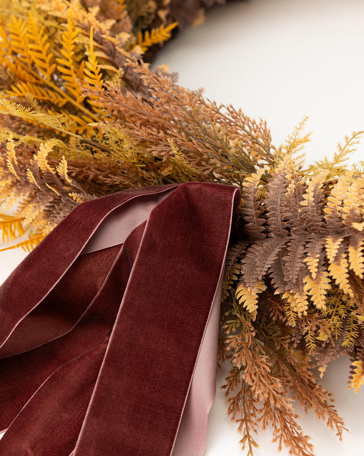 A close-up of the 30 Faux Golden Fern Wreath, featuring yellow and brown faux ferns with a dark red velvet ribbon, perfect for fall entryway decor against a white background, by McGee & Co.