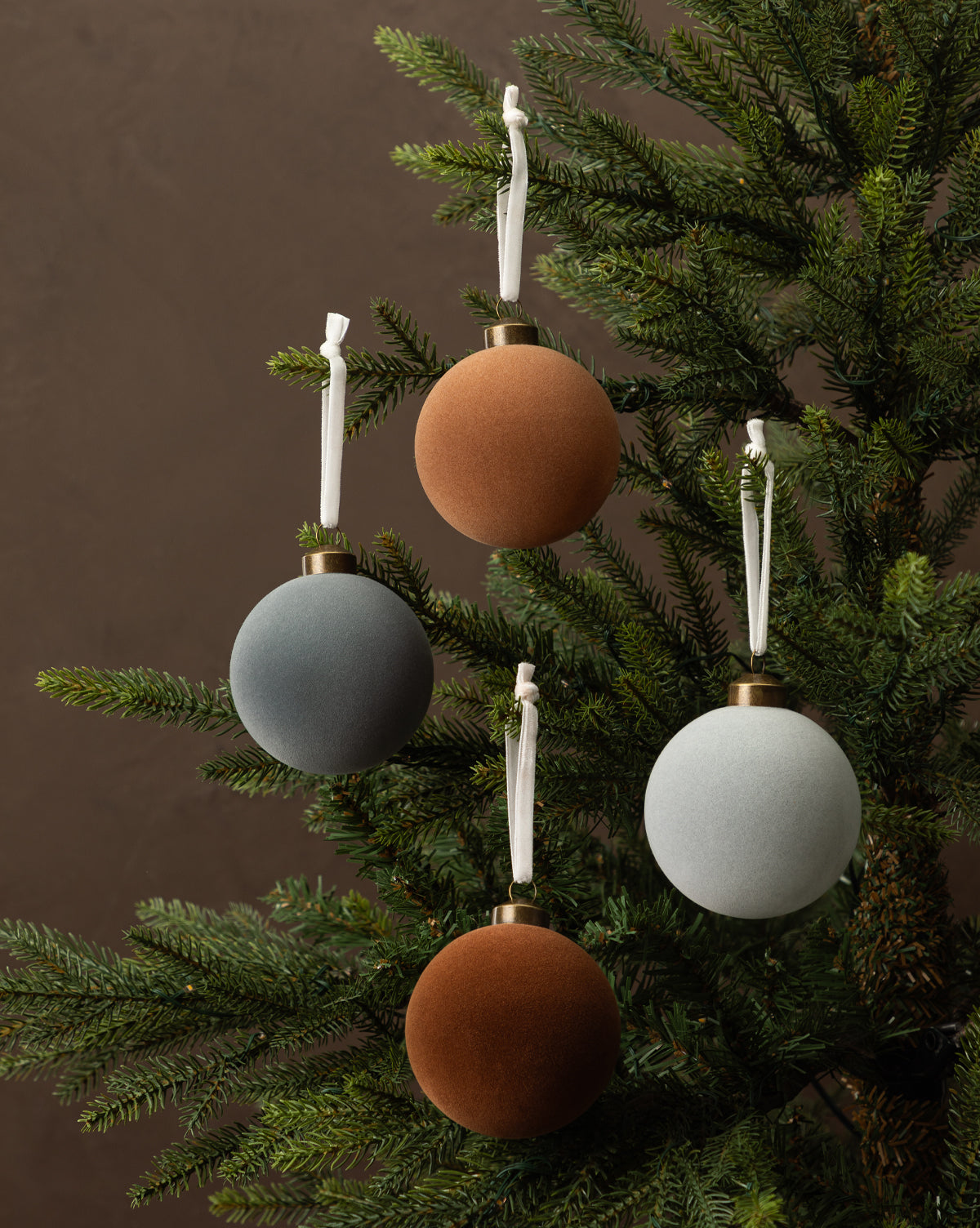 The 3" Assorted Flocked Baubles (Set of 4) features round, matte-finish ornaments in brown, rust, gray, and blue-gray with white hanging ribbons—perfect for adding a stylish touch to your holiday décor, by McGee & Co.