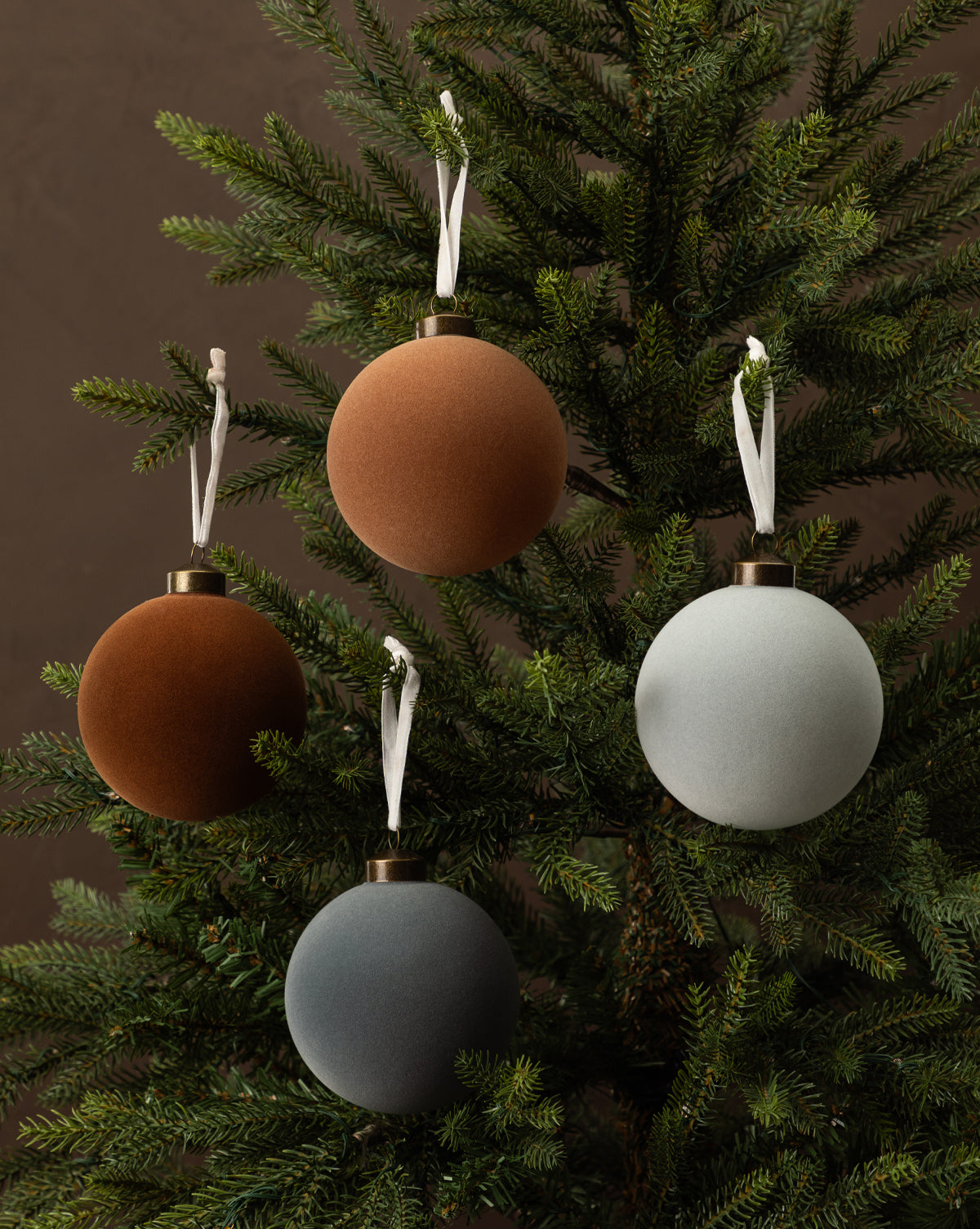 The 4" Assorted Flocked Baubles (Set of 4) features velvet-textured ornaments in gray, light blue, rust, and taupe with white hanging ribbons, perfect for adding an elegant touch to your holiday décor, by McGee & Co.