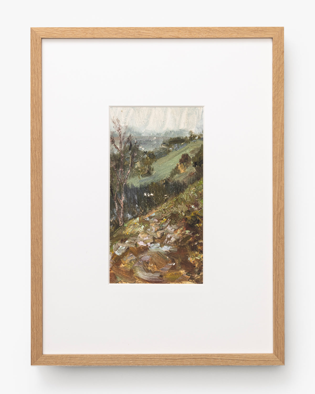 A framed painting titled A River Runs Through features a small, vertical landscape of grassy hills, trees, and rocks beneath a cloudy sky in earthy green and brown tones with a light wood frame and white mat, by McGee & Co.
