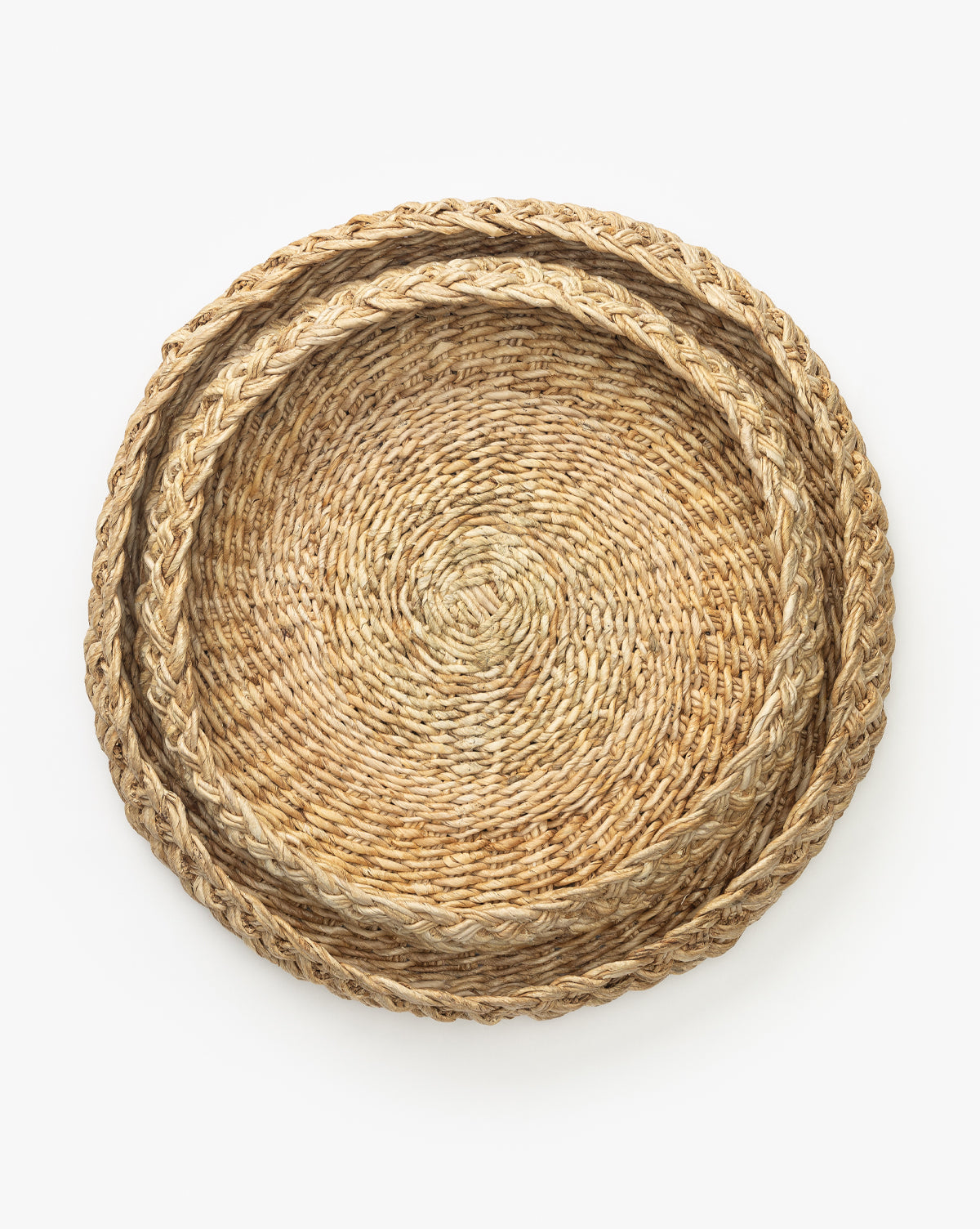 The Abaca Braided Rope Tray set includes two round, woven wicker baskets, one nested inside the other. Displayed on a white background, these trays feature natural abaca texture with braided rope edges for rustic charm by McGee & Co.