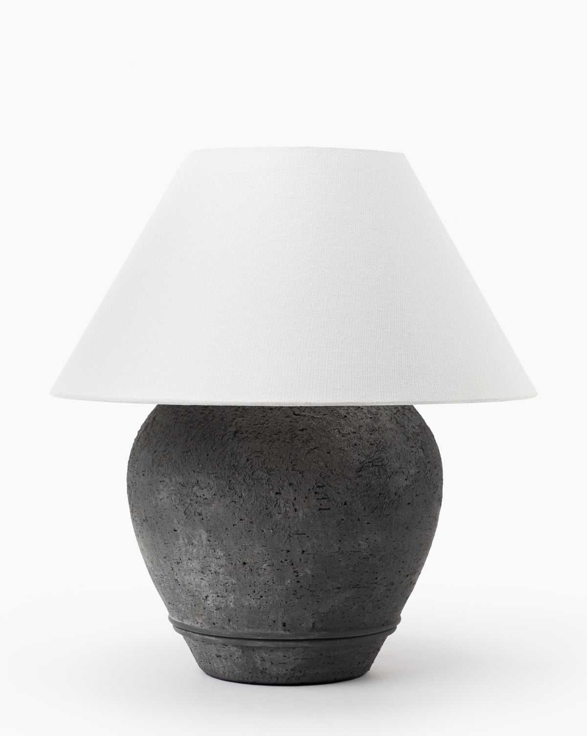 The Abbott Ceramic Table Lamp features a textured dark gray round ceramic base and a wide white linen shade, shown against a plain white background, by McGee & Co.