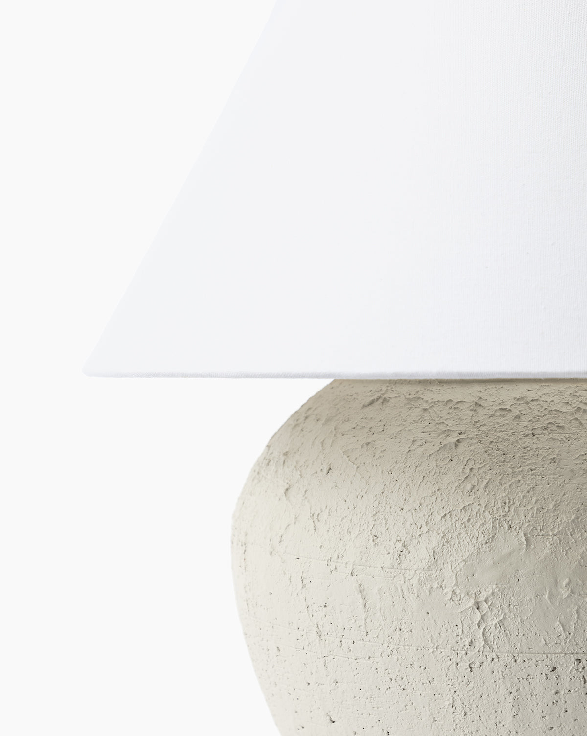 Close-up of the Abbott Ceramic Table Lamp, showcasing its textured, round ceramic base and the lower edge of a white linen shade against a plain white background, by McGee & Co.
