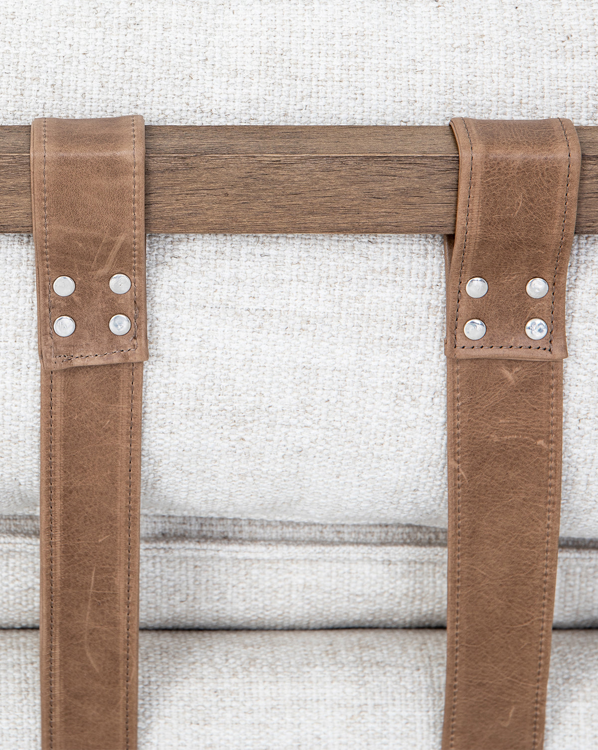 Close-up of taupe leather buckles with metal rivets on the Aberdeen Day Bed’s parawood frame, displayed against a textured light beige fabric background, by McGee & Co.