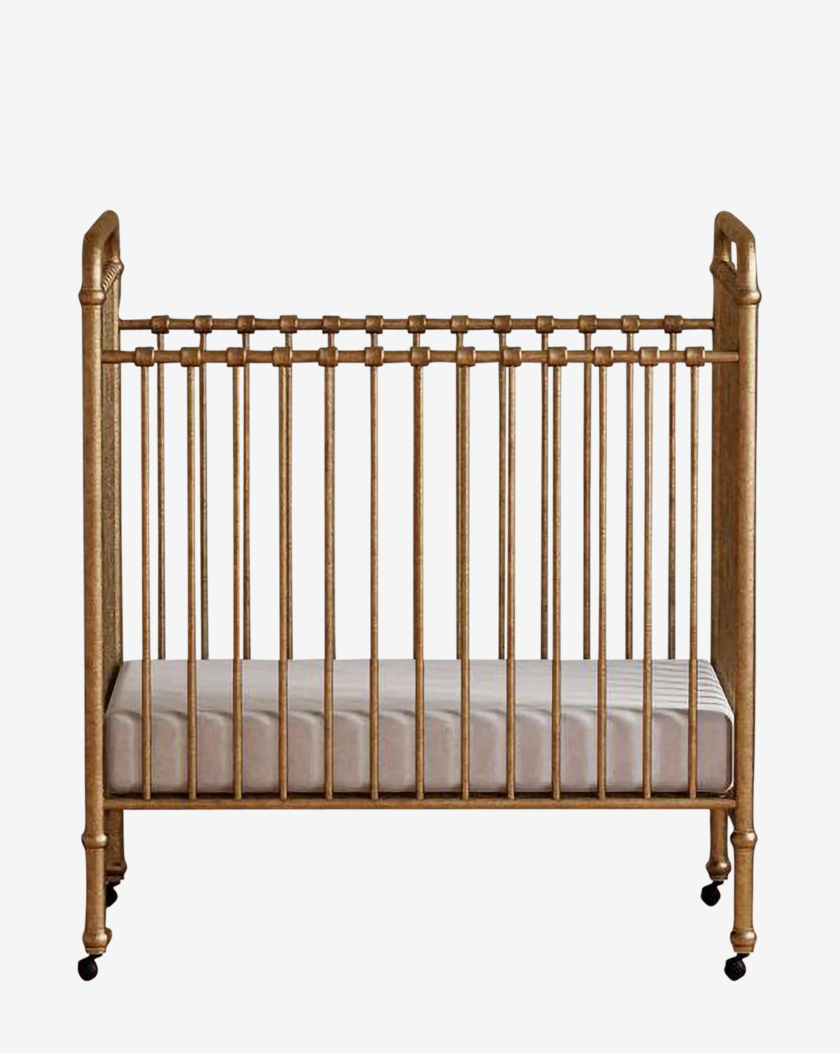 The Abigail Mini Crib by Million Dollar Baby is a gold-colored vintage crib featuring vertical slats, decorative rounded corners, a white mattress, and small black wheels, displayed against a plain white background. McGee & Co.