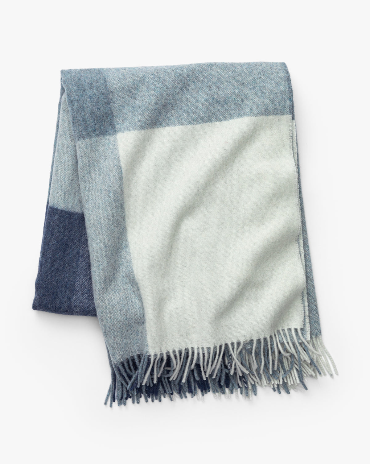 The Abner Throw by Fibre is an eco-friendly blanket made from recycled alpaca wool, featuring large light blue, gray, and cream checkered blocks with fringed edges by McGee & Co.