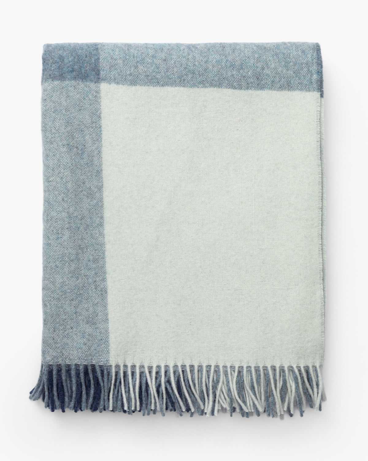 The Fibre Abner Throw is a folded, eco-friendly blanket with a simple block pattern in light blue and off-white, finished with fringe along the bottom edge. McGee & Co.