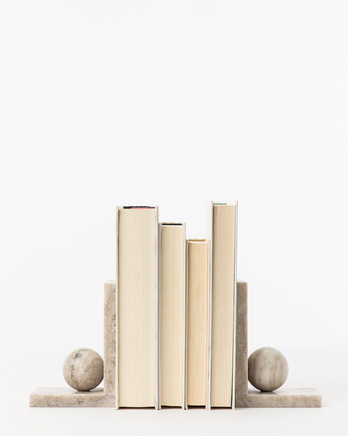 Five books of different heights are positioned upright between the Adar Marble Bookends (Set of 2), which feature spherical stones on rectangular bases, all set against a plain white background.