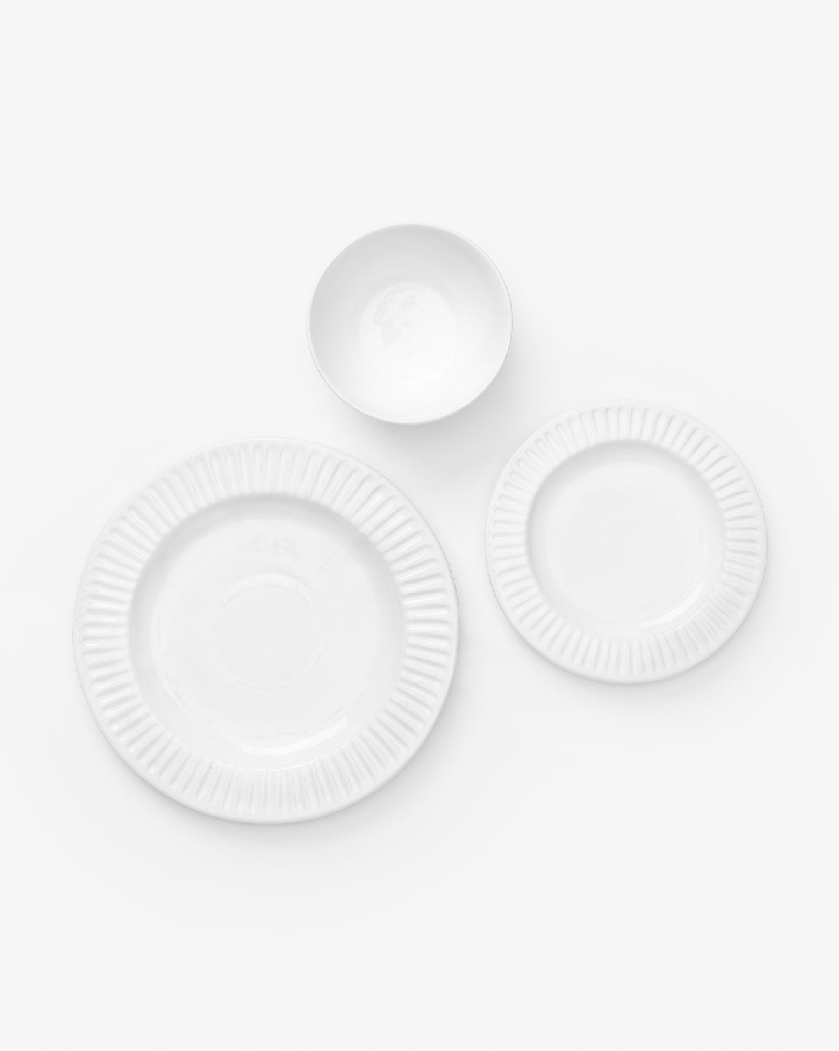 Four Adele White Dinner Plates are arranged in a loose triangular pattern on a white background, showcasing their classic ribbed edge and timeless ceramic design, by McGee & Co.