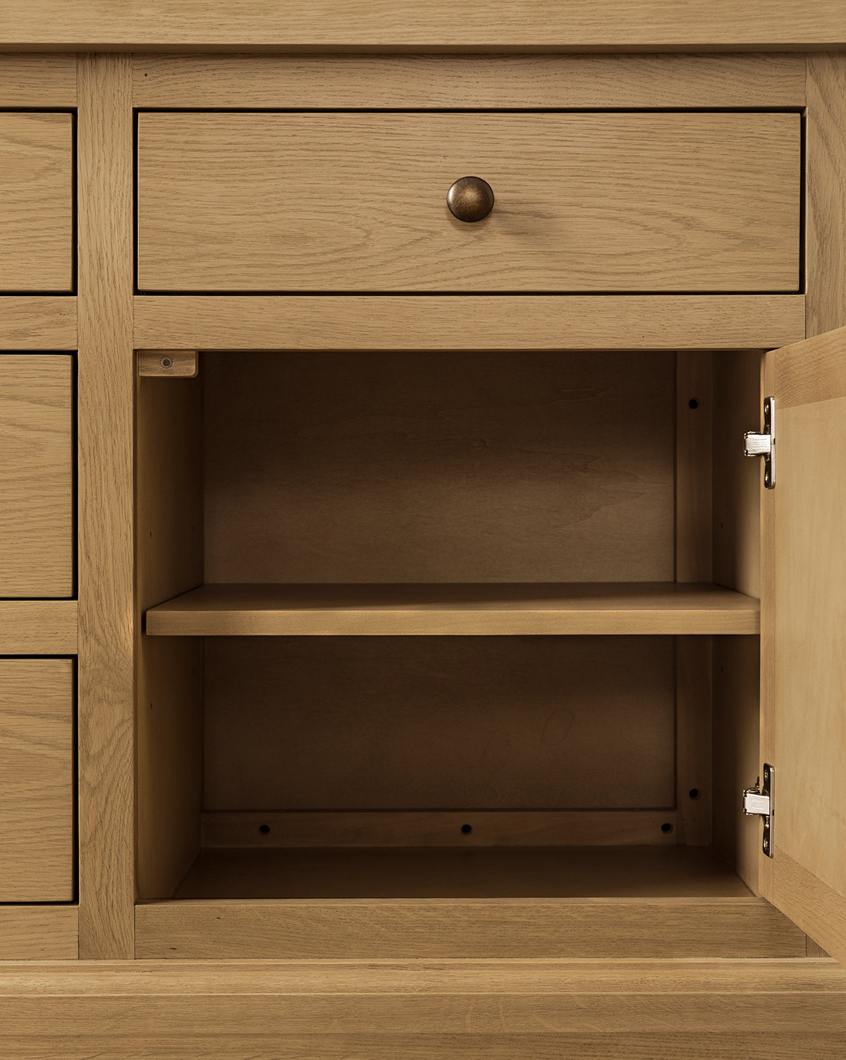 The Adler Oak Cabinet features a light oak finish with an open door revealing spacious interior shelving, while a closed drawer above with a round metal knob enhances its practical design, by McGee & Co.