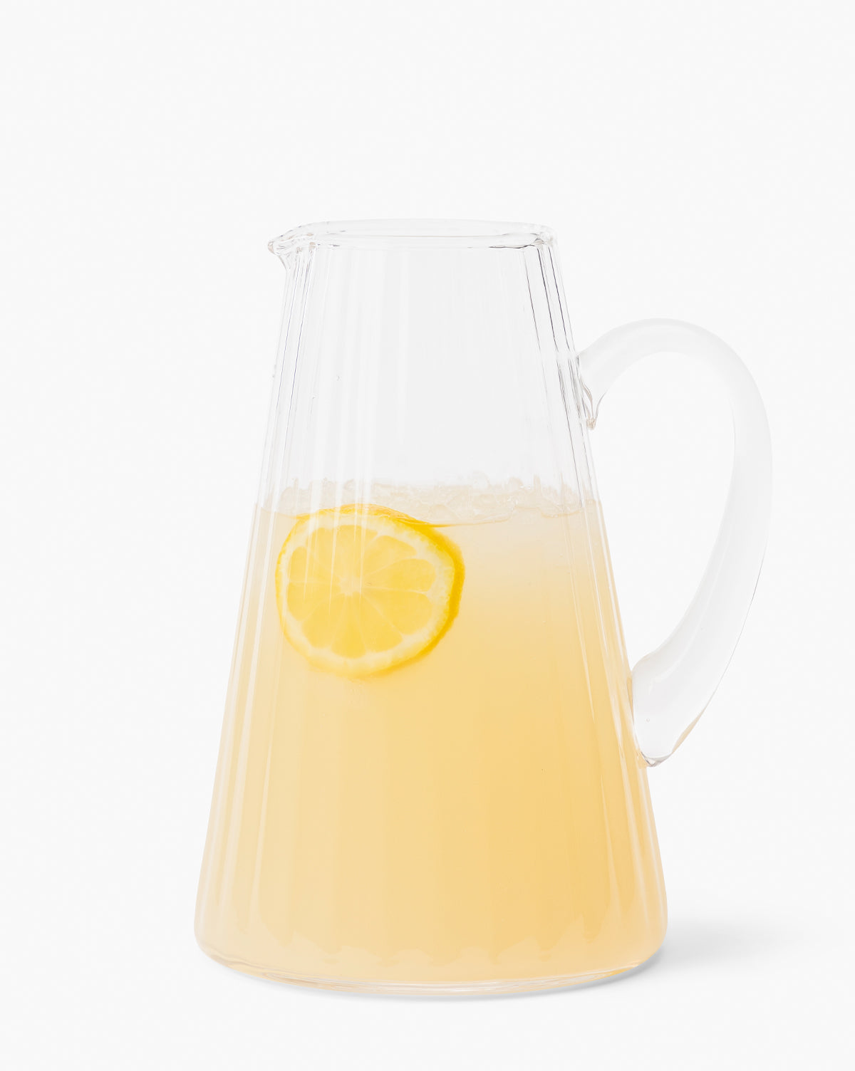 The Adonis Ribbed Glass Pitcher, filled with pale yellow lemonade and a lemon slice floating inside, sits against a plain white background—ideal for effortless kitchen styling, by McGee & Co.