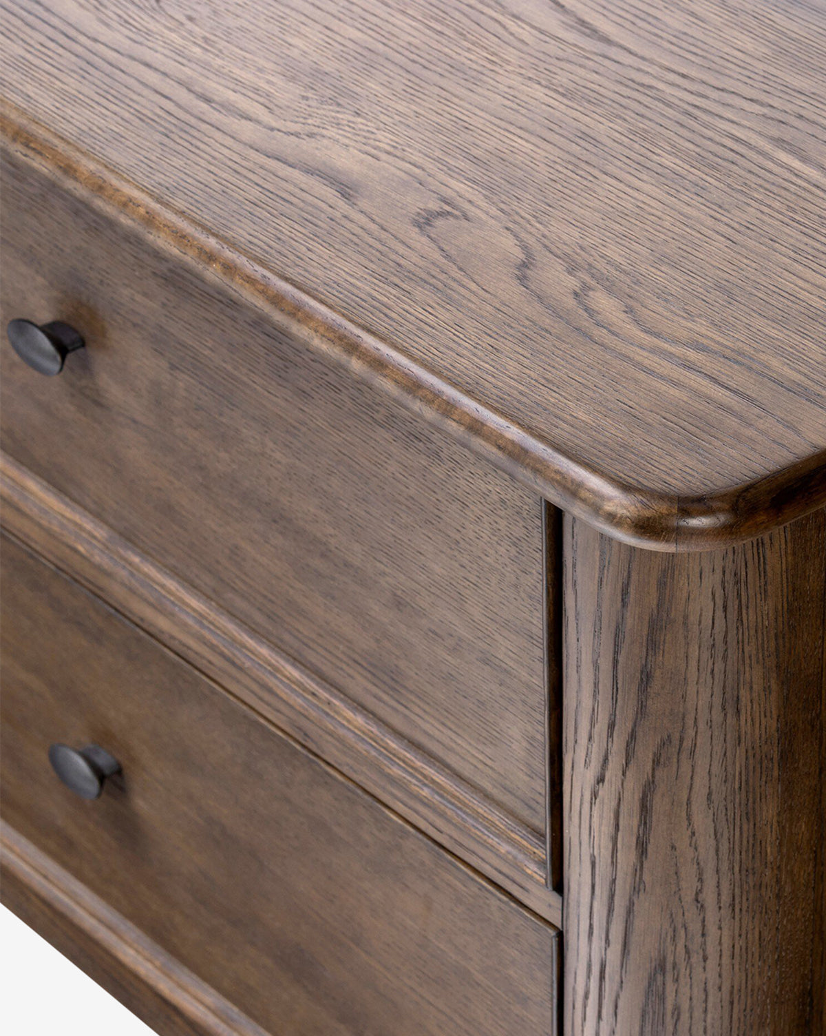 Close-up of the top corner of the Aeris Nightstand reveals a smooth, natural wood grain finish. Two drawers with black round knobs provide bedroom storage. The nightstand features rounded edges and a rustic look, by McGee & Co.