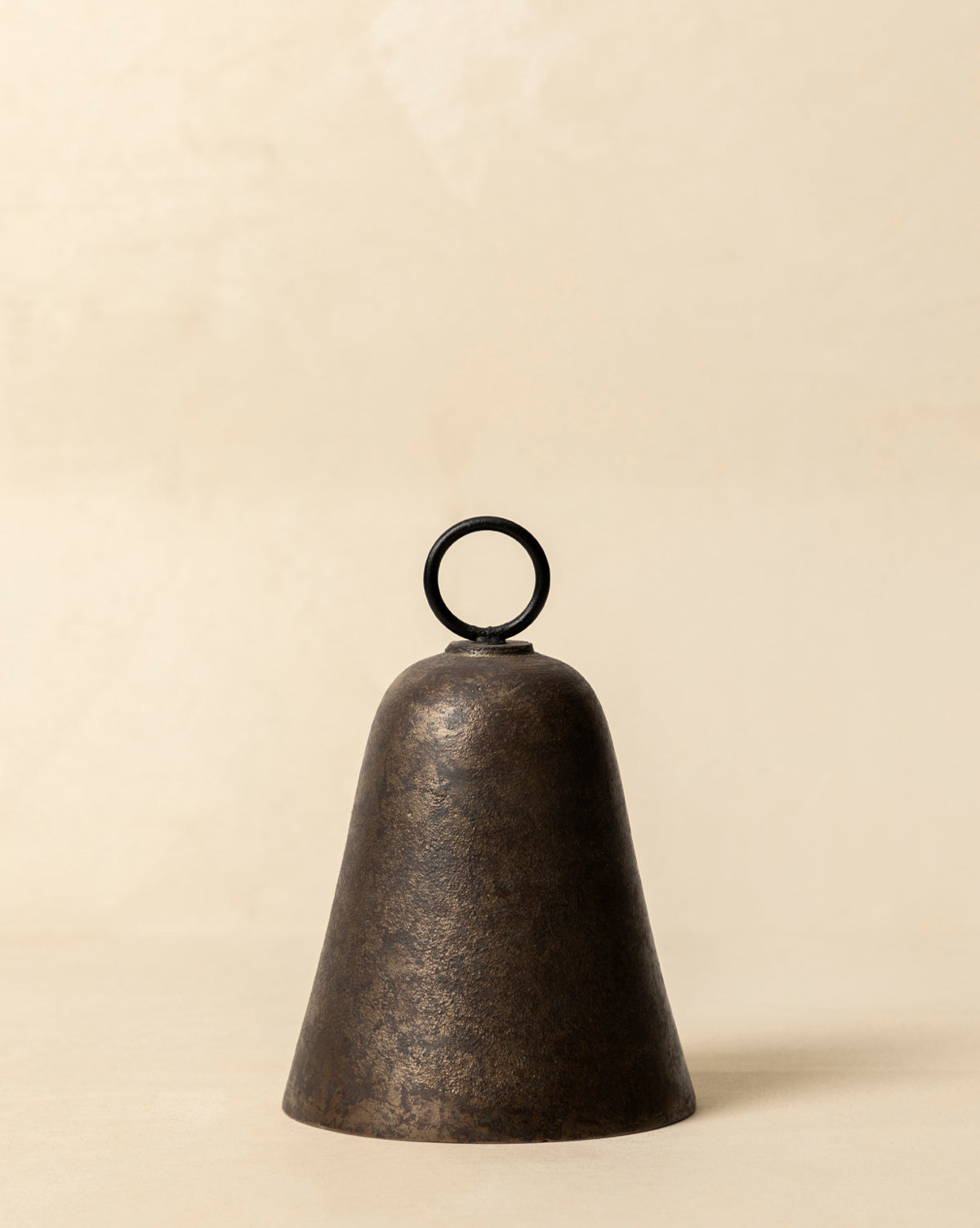 The Aged Brass Bell, featuring a dark finish and round top handle, rests on a light beige surface, bringing vintage charm to the simple background, by McGee & Co.