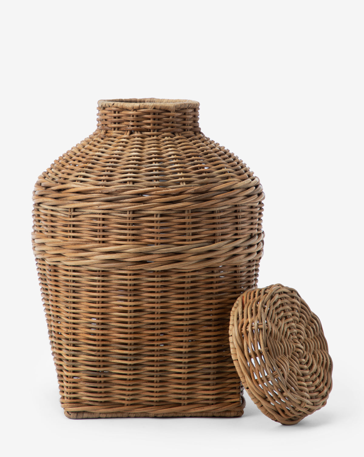 The Ahnamia Wicker Jar, a large square woven basket with a cylindrical neck and matching round lid, is empty and displayed against a white background. The lid rests on the ground next to the jar, highlighting its vase-like design.