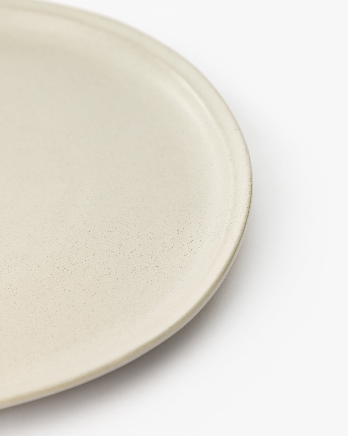 Close-up of the Aiden Soft Gray Dinner Plate, a round glazed ceramic with a smooth surface, shown partially on the left against a white background, by McGee & Co.
