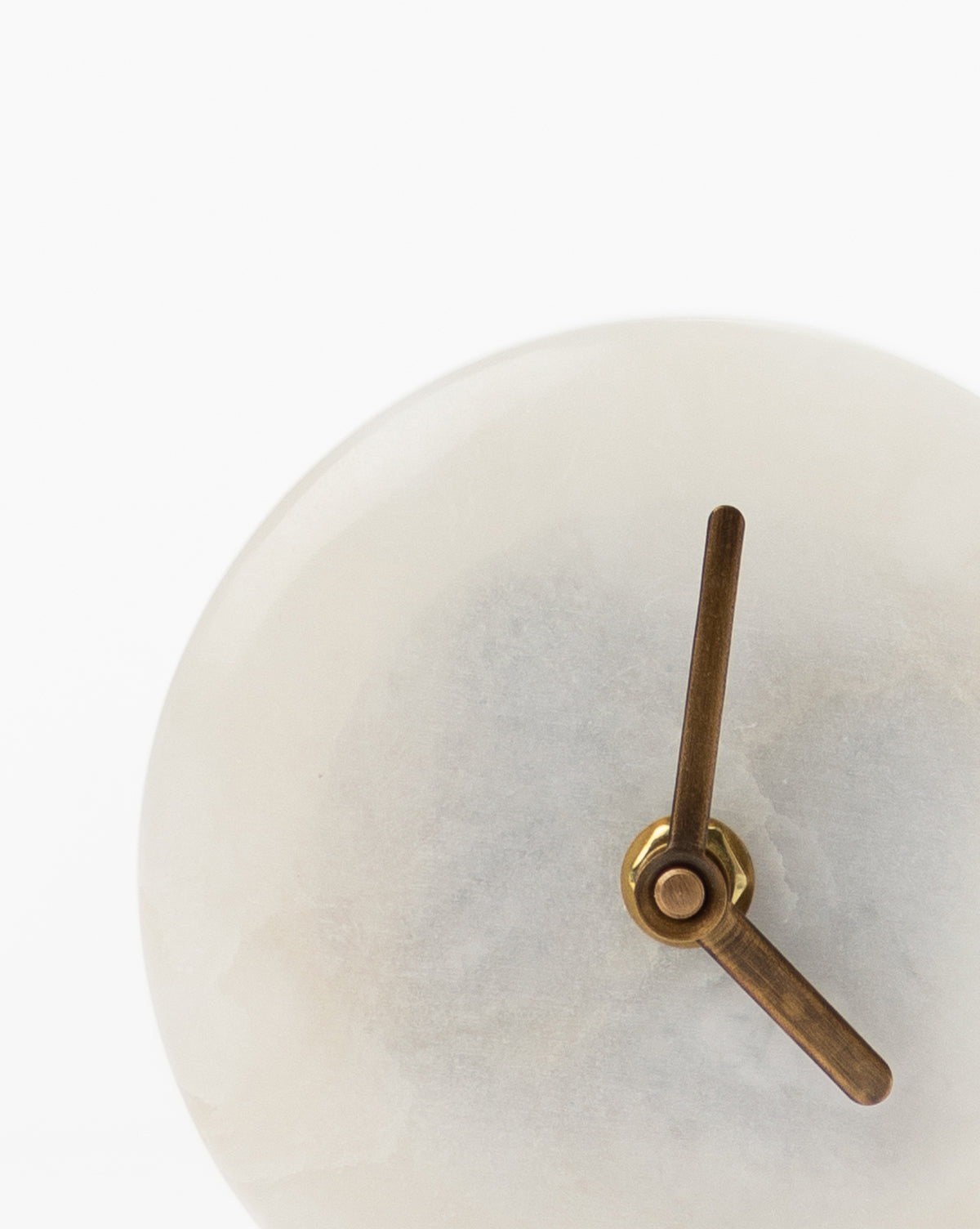 Minimalist close-up of the Alabaster Table Clock, featuring a white marble face and gold hands, set against a plain white background. Only part of this elegant design is visible in the frame.