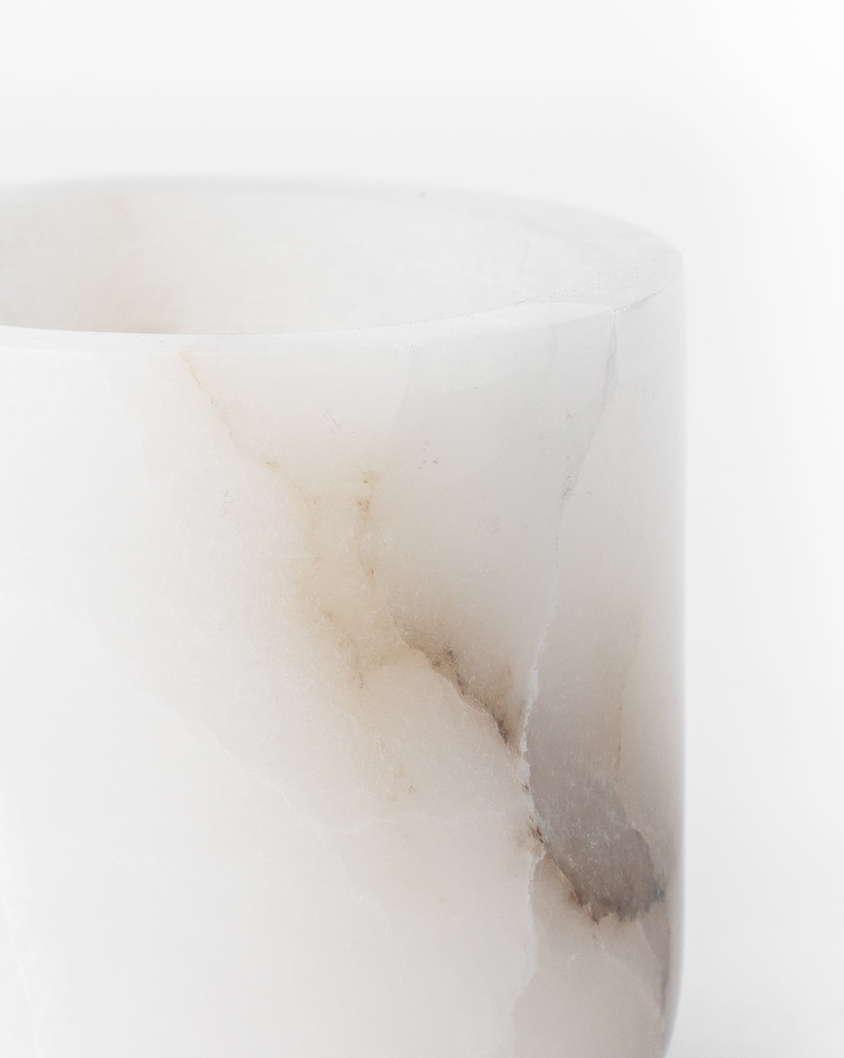 A close-up of the Alabaster Tea-light Holder, a cylindrical white marble piece with natural beige and gray veining, displayed against a plain white background.