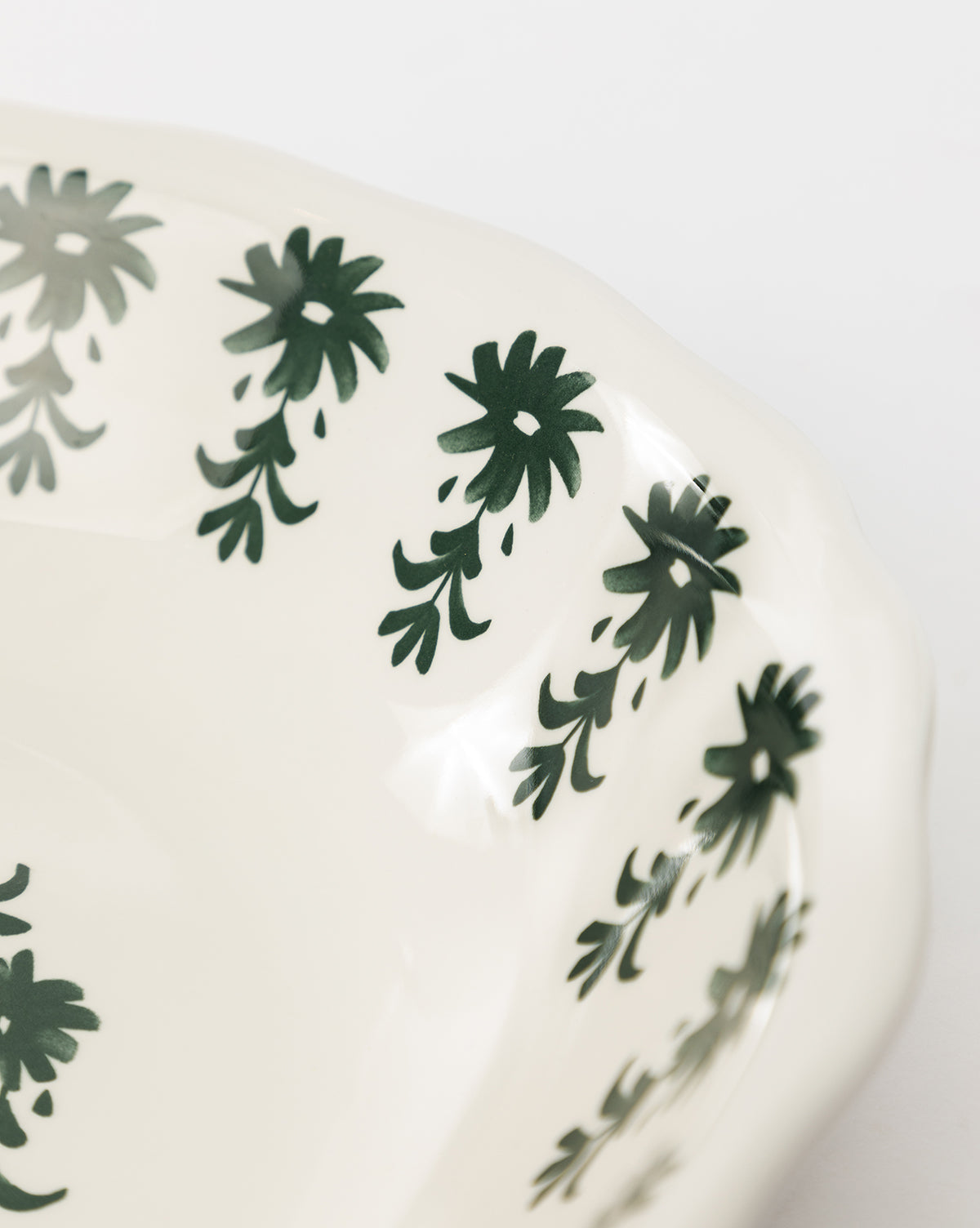 A close-up of the Alba Melamine Serving Bowl, featuring a white finish, scalloped edge, and a dark green floral motif along the rim, by McGee & Co.