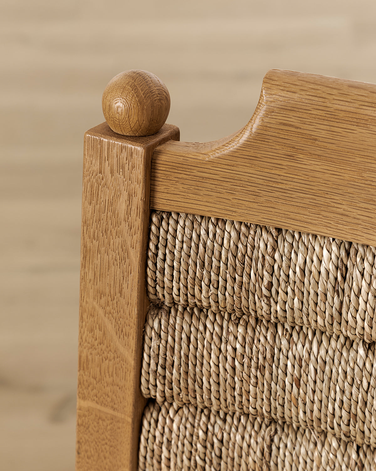 Certainly! Here’s your revised description with the exact string “McGee & Co.” blended seamlessly at the end: Close-up of the honey oak Makerspalm Alberta Counter Stool’s top corner, showing a rounded finial and woven rattan backrest against a blurred, light background. McGee & Co.