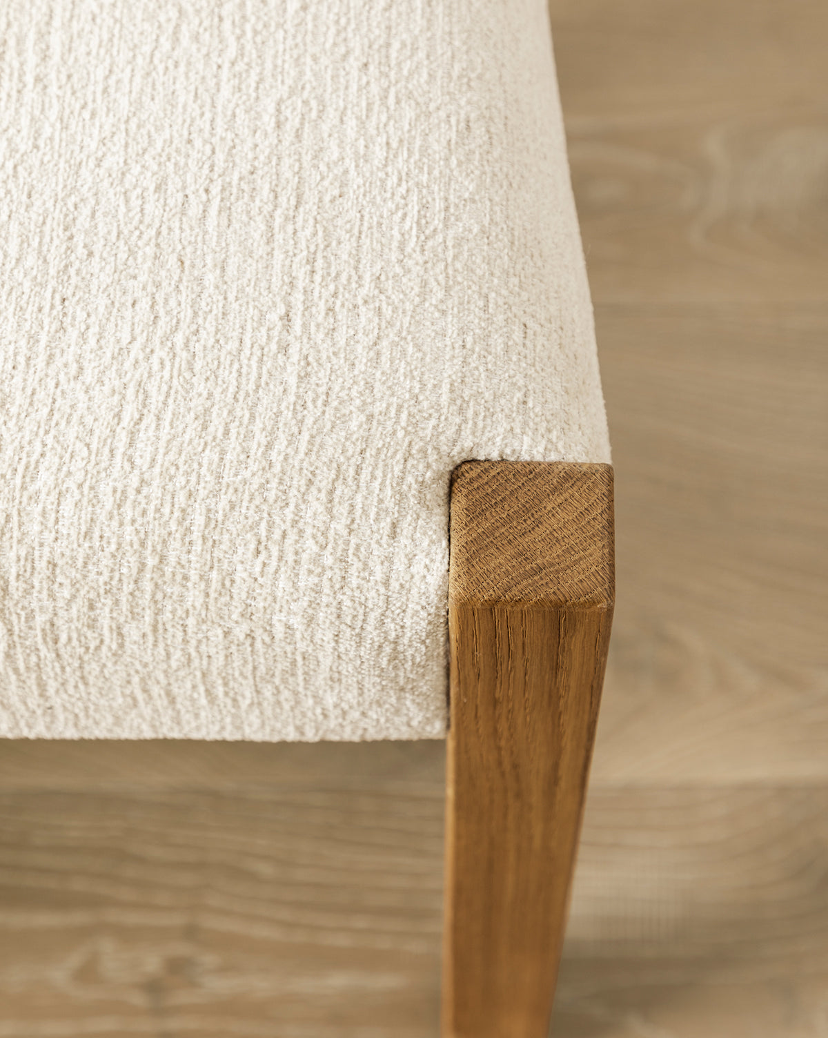 Close-up of the Alberta Dining Chair featuring textured, cream-colored upholstery and a wooden leg, set on a light wood floor, by McGee & Co.