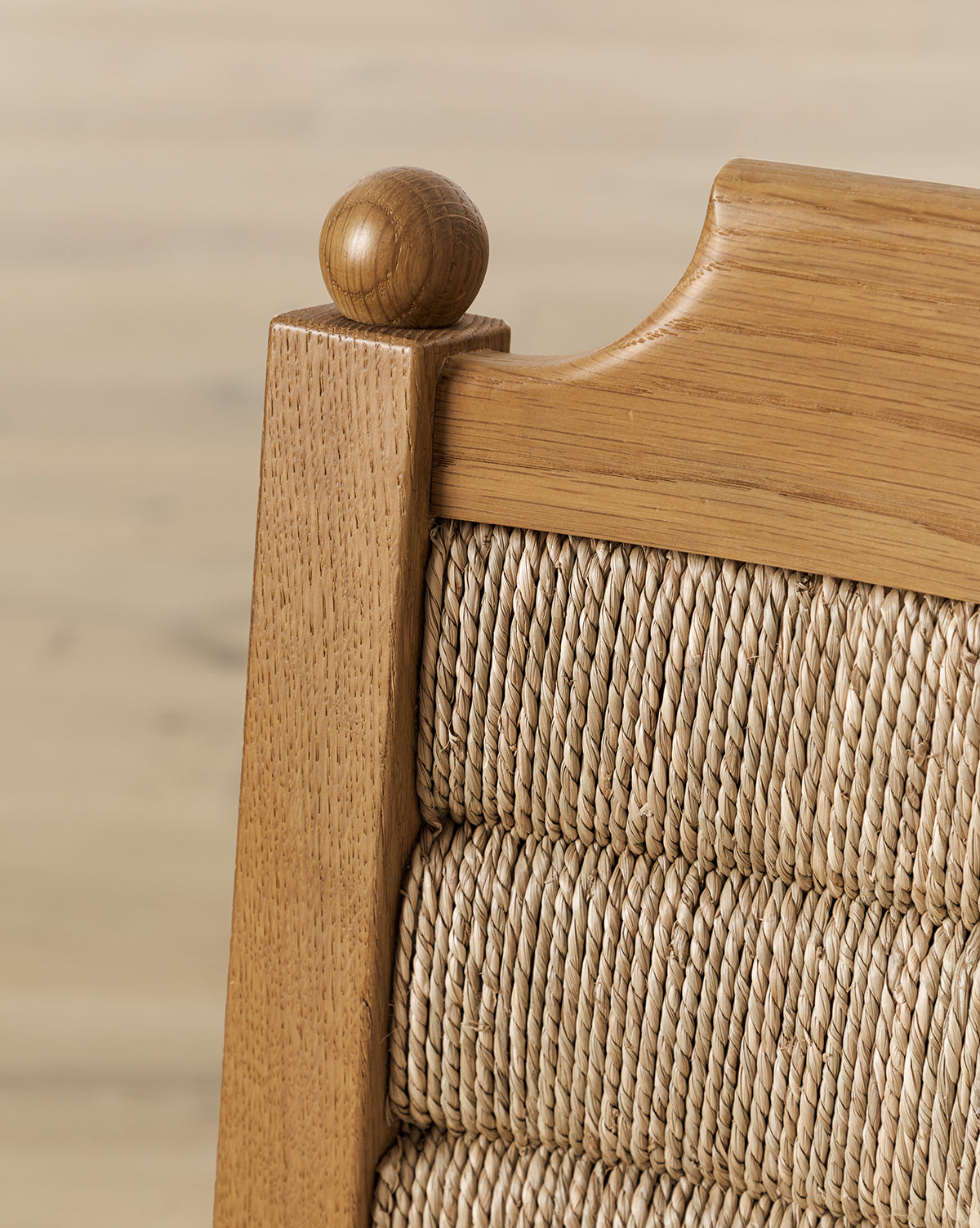 Close-up of the top corner of the Alberta Dining Chair with a rounded finial, showcasing woven wicker detailing on the seat back. The blurred wood flooring background accentuates this elegant piece, by McGee & Co.