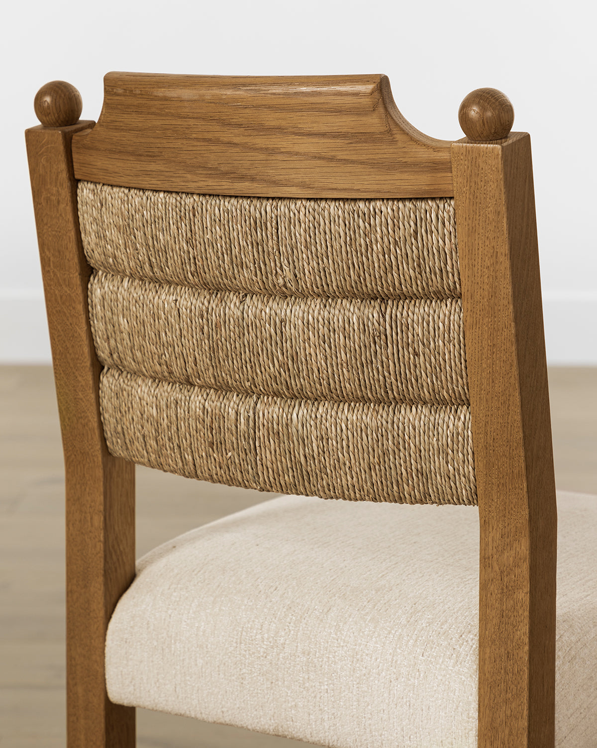 The Alberta Dining Chair features a curved backrest with three horizontal rows of woven rope and a cream upholstered seat, shown here on a light wood floor, by McGee & Co.