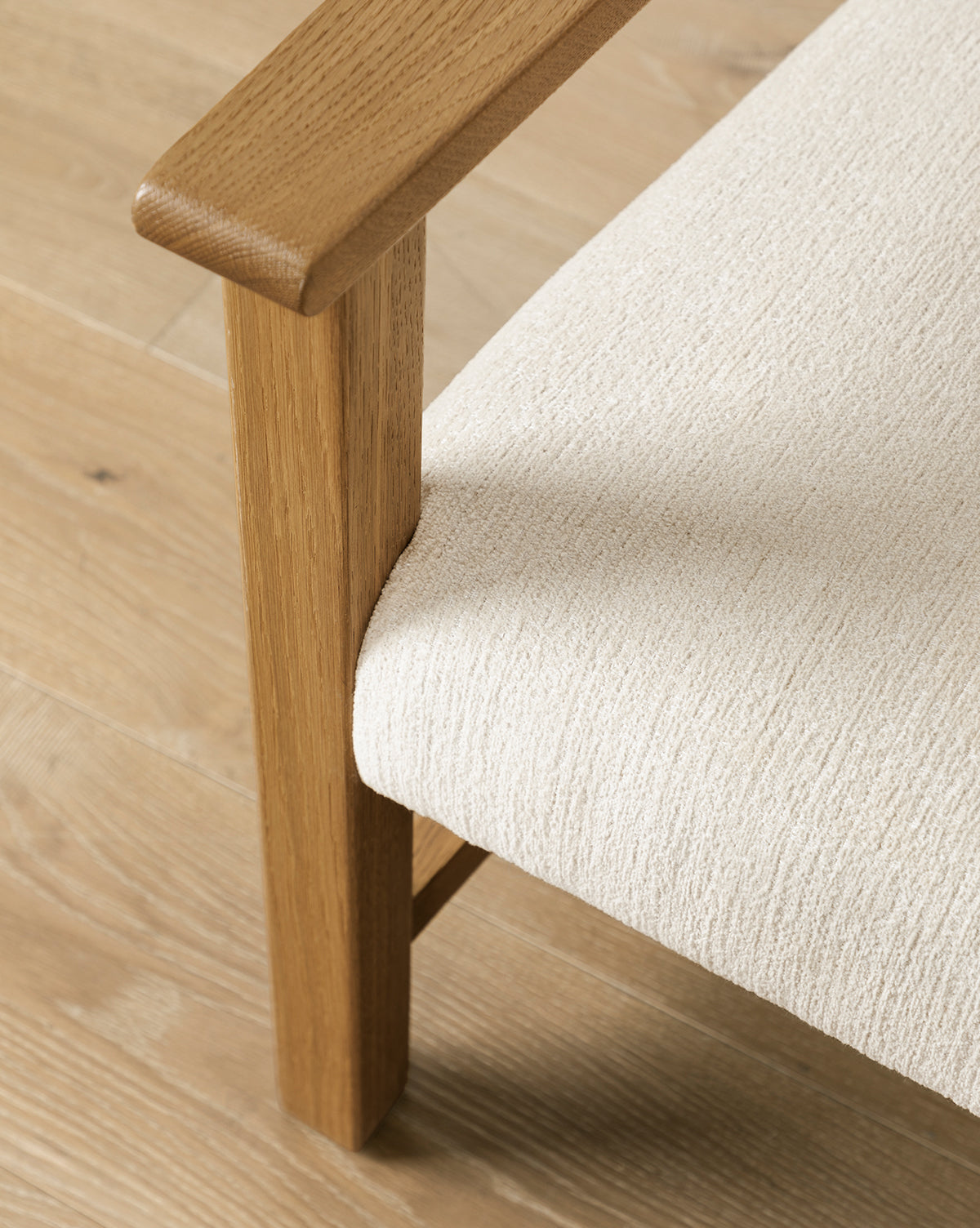 Close-up of the Alberta Lounge Chair’s wooden armrest and leg with a textured off-white upholstered seat on a light wood floor—ideal for vintage-inspired décor lovers, by McGee & Co.