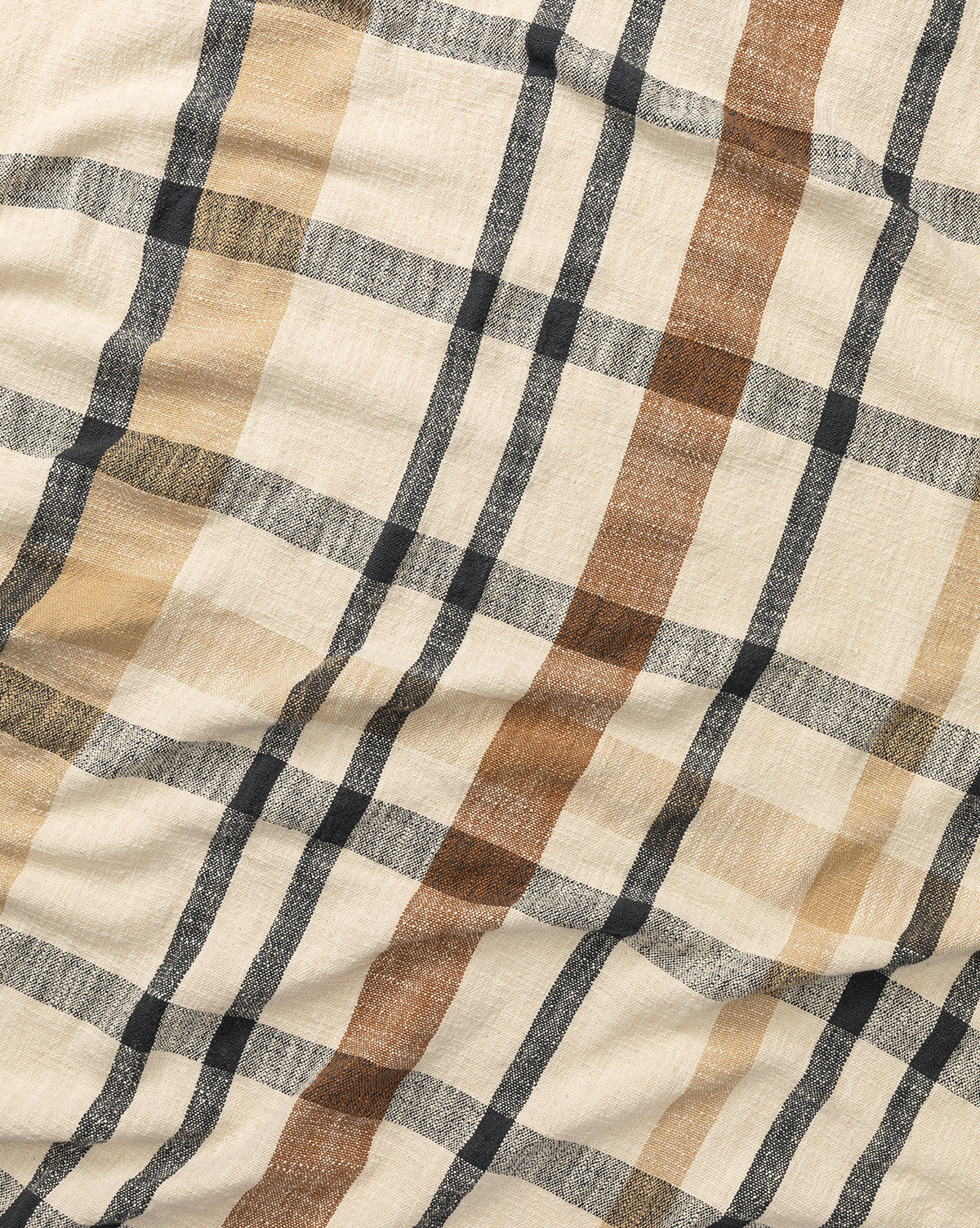 The Raj Albright Plaid Throw is a beige cotton throw with a crinkled texture and a plaid pattern in black, brown, and tan stripes. McGee & Co.