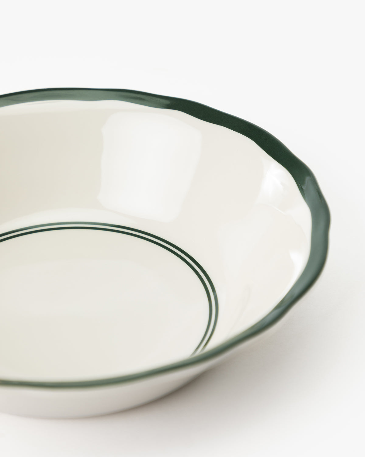 A close-up of a white Alcott Melamine Bowl from the set of 4, showcasing its scalloped edge, dark green rim, and two green lines around the inner base, set against a plain white background by McGee & Co.