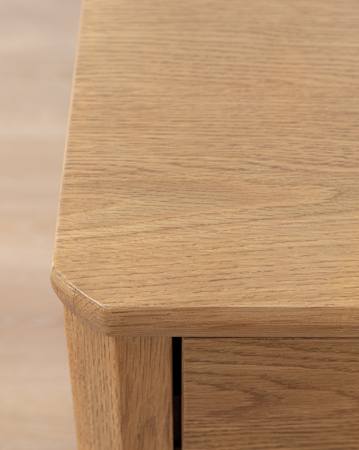 Close-up of the Alessandra Nightstand’s corner, featuring solid oak construction, a smooth finish, visible wood grain, and a beveled edge. The blurred background highlights the nightstand’s surface and craftsmanship by McGee & Co.