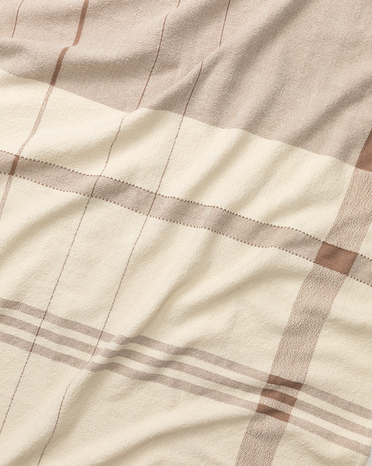 A close-up of the ILA HOME FASHIONS Alex Plaid Throw highlights its soft texture and gentle wrinkles in neutral beige, cream, and thin brown stripes—an inviting, luxurious throw blanket for any space. McGee & Co.
