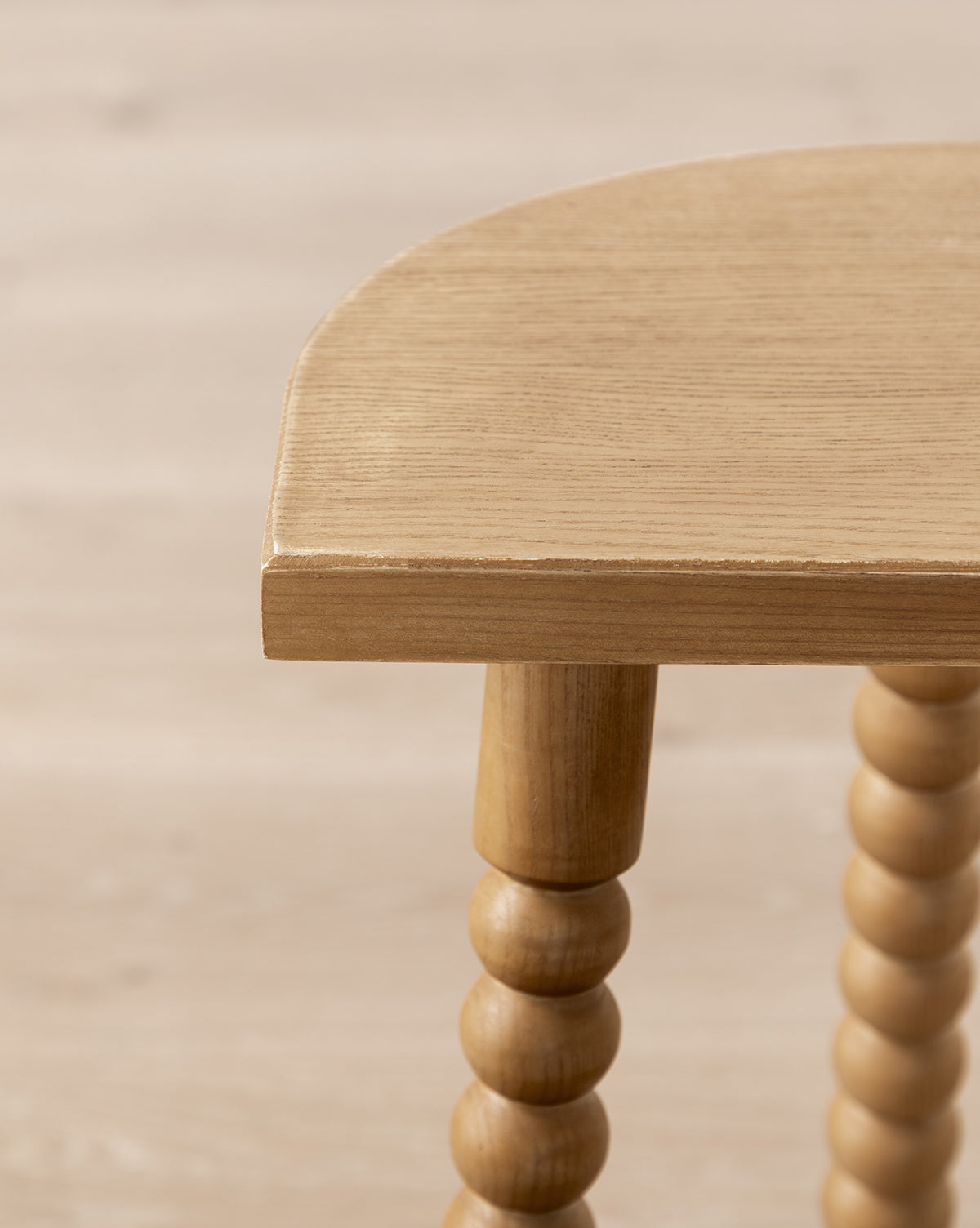 Close-up of the Makerspalm Alice Honey Wood Stool, featuring a rounded edge, spindle-style legs, and a light natural finish that highlights its craftsmanship, adding timeless charm to any space. McGee & Co.