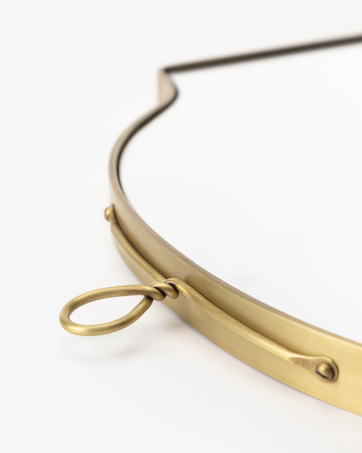 Close-up of the Allegheny Wall Mirror, featuring a gold-colored metal frame, curved edge, and oval hanging loop, set against a white background by McGee & Co.