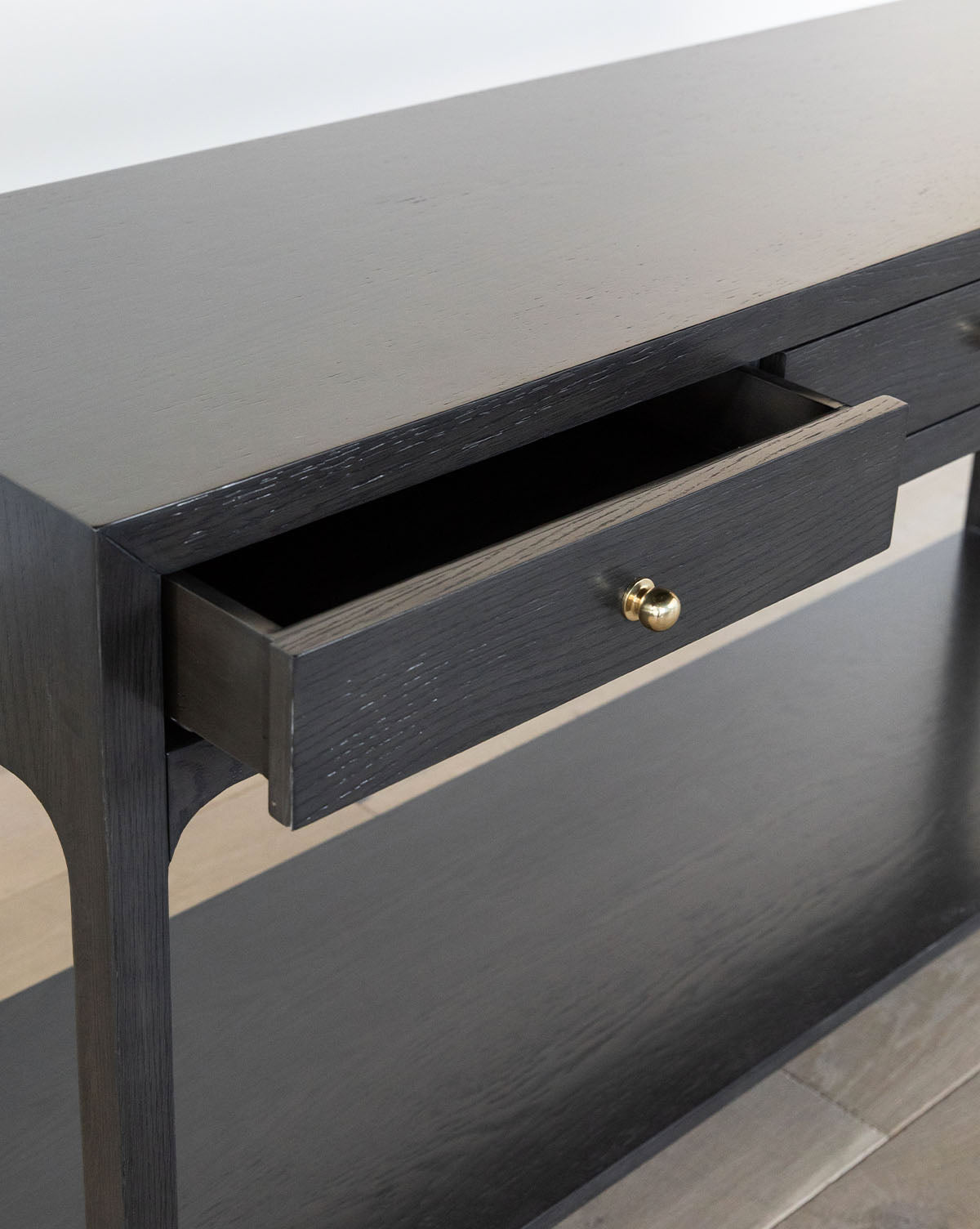A close-up of the Allen Black Console in dark wood, featuring a single partially open drawer with a round brass pull, lower shelf, and light wood flooring underneath, by McGee & Co.