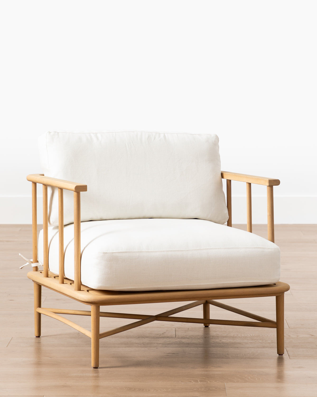 The Alma Lounge Chair features a modern design with comfortable white cushions and a light wood frame, set on a hardwood floor against a plain white background, by McGee & Co.